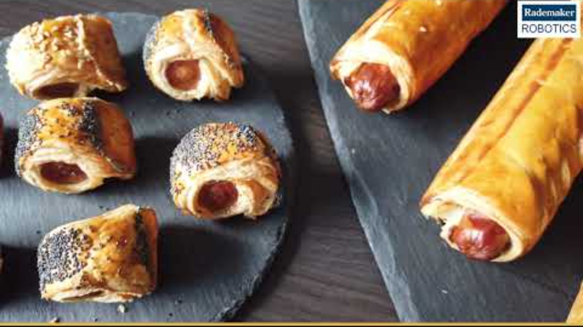 A slate serving tray with several sausages wrapped in puff pastry, some with seeds, next to two larger sausages wrapped in puff pastry. A Rademaker Robotics logo appears in the top right corner.