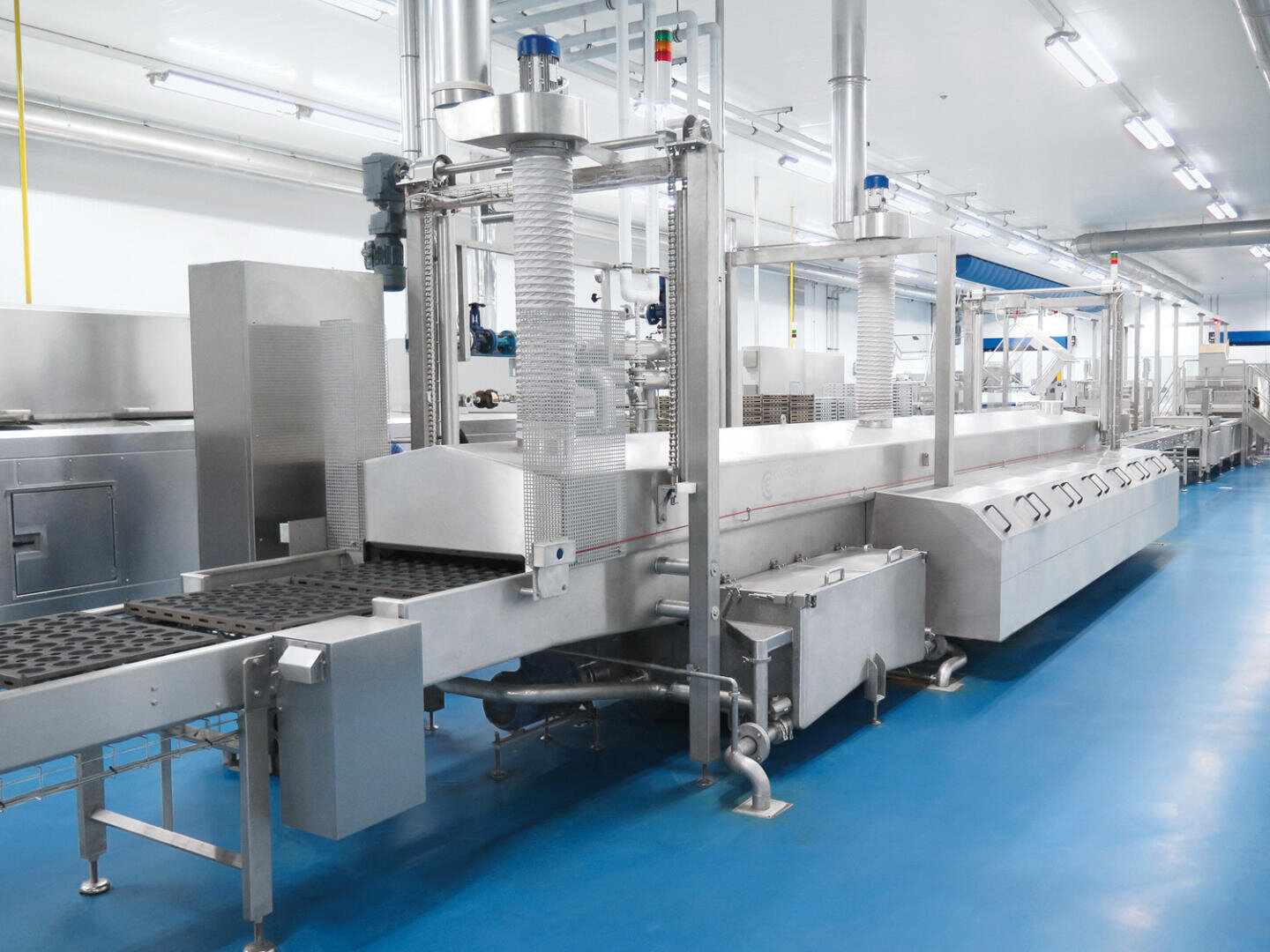 Ein modernes Fördersystem aus Edelstahl zur Lebensmittelverarbeitung in einer sauberen, hell erleuchteten Industrieanlage mit blauen Böden und Deckenbeleuchtung.