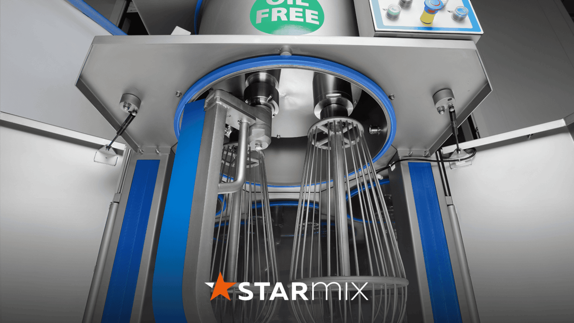 Close-up view of a large industrial mixing machine with metal whisks inside, labeled OIL FREE at the top. Control buttons are visible on the right, and the STARMIX logo appears at the bottom.