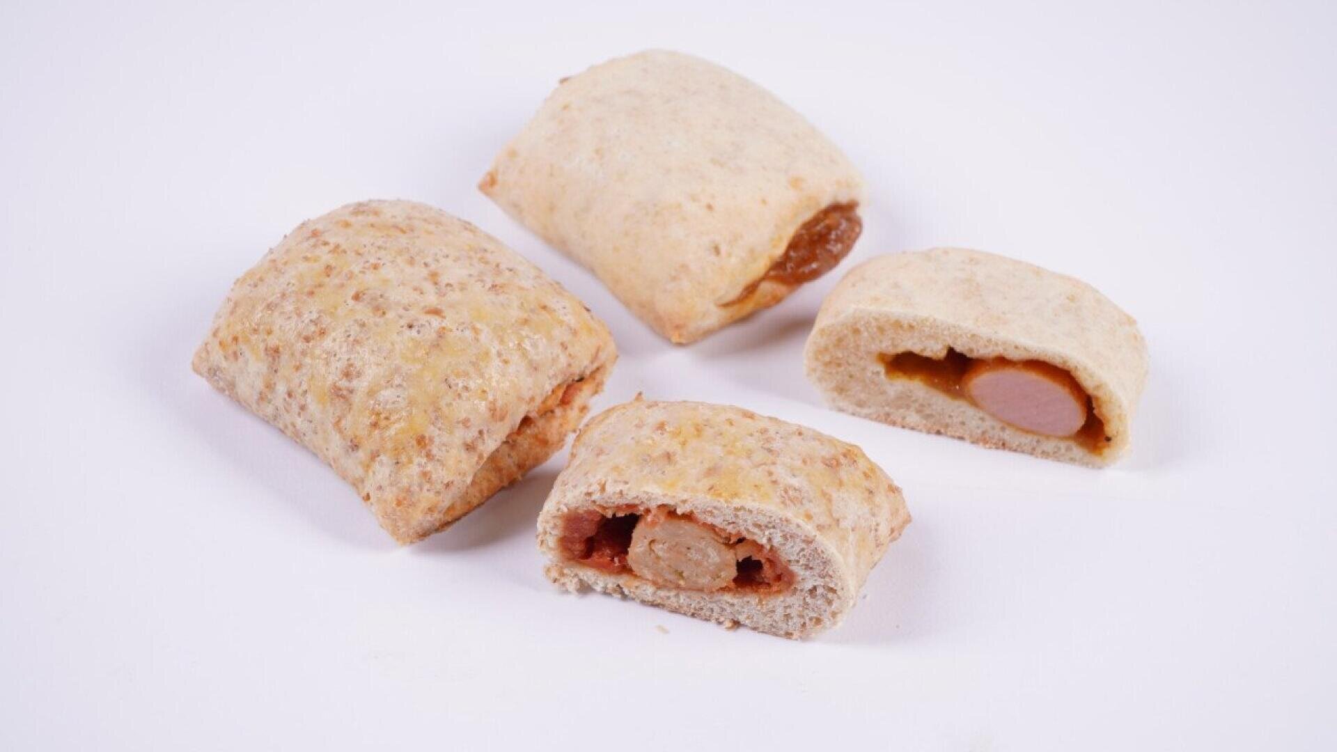 Four whole grain bread pockets, two of which are sliced open to reveal a sausage and sauce filling, are arranged on a white background.