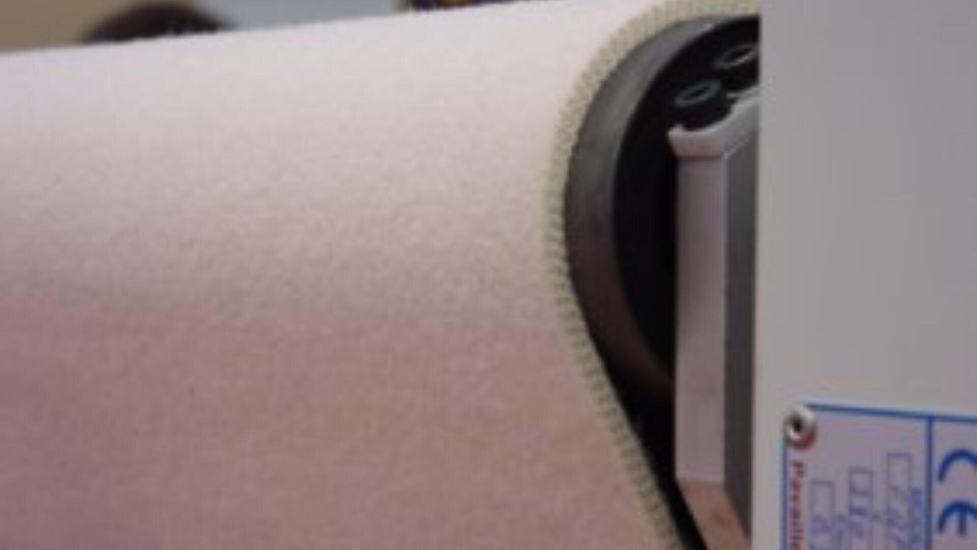 Nahaufnahme einer großen Rolle hellen Gewebes, das in einer Industriemaschine verarbeitet wird.