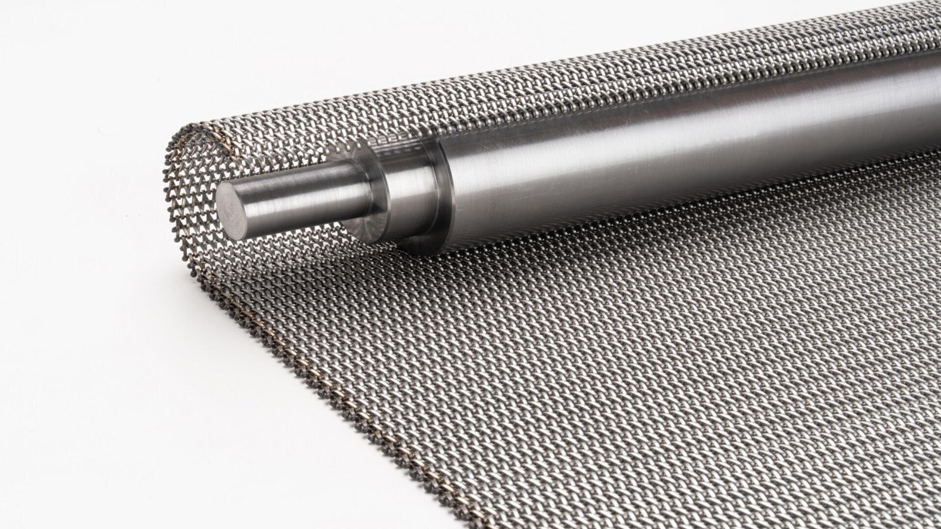 A roll of fine metal mesh with a smooth cylindrical metal rod at the core, partially unrolled on a white surface.