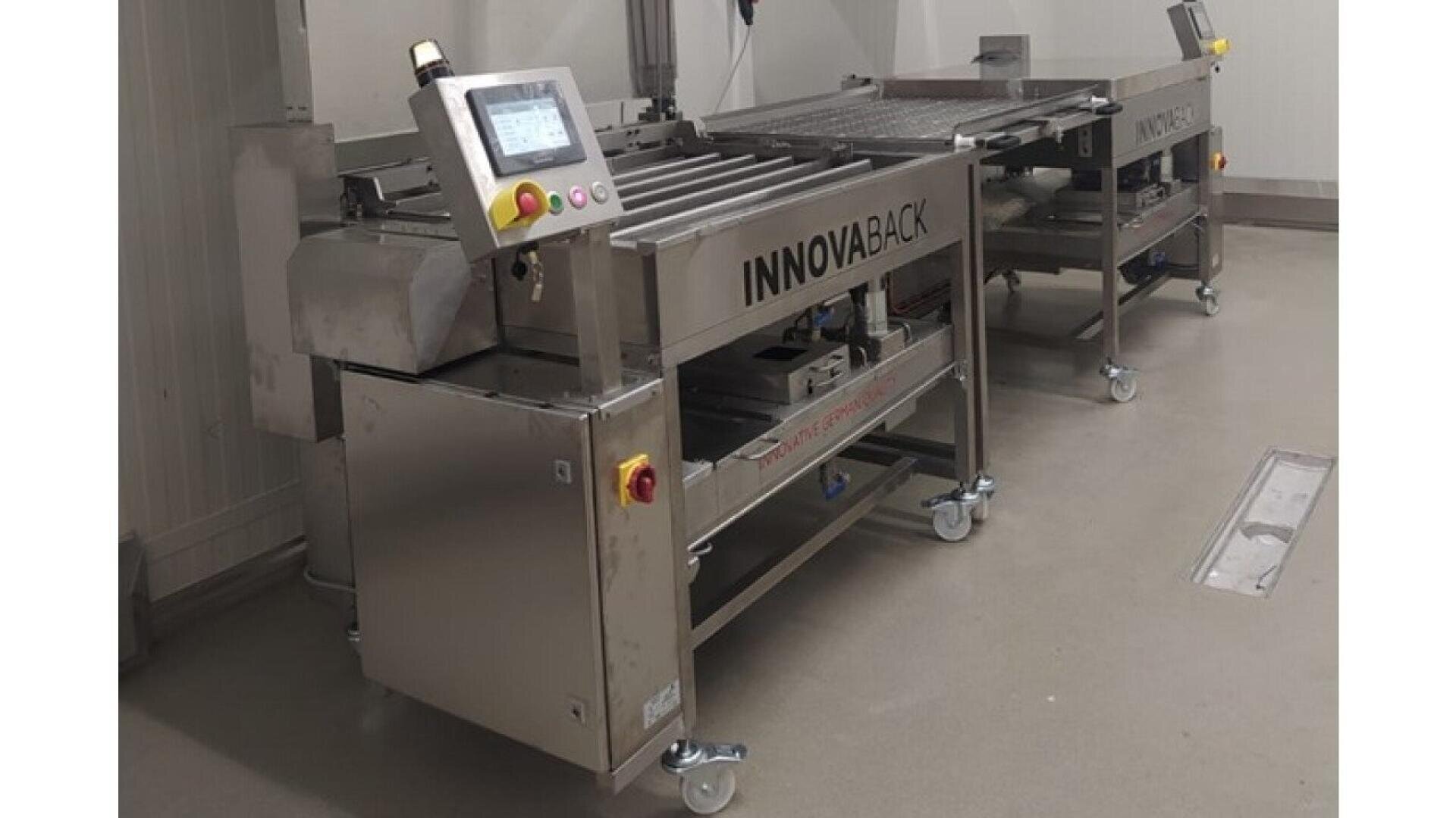 A stainless steel industrial machine labeled INNOVABACK with a control panel and rollers, positioned in a clean, indoor facility with a smooth, light-colored floor.