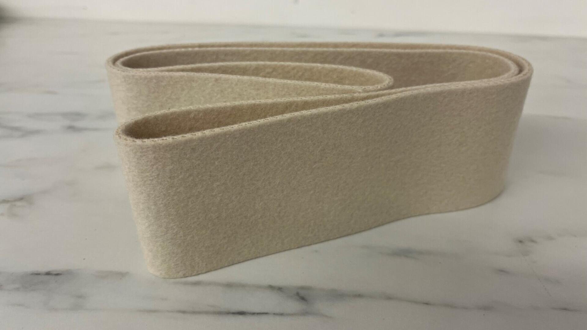A beige, felt-like fabric strip is folded in a flat, looped shape on a light marble surface.
