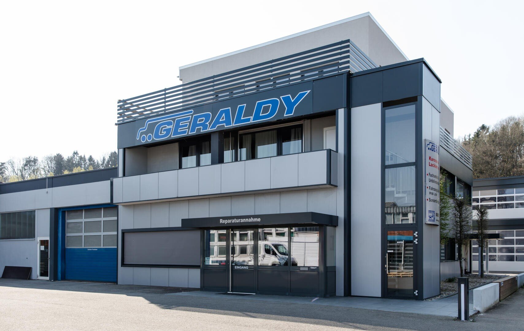 Modernes Kfz-Werkstattgebäude mit einem großen blauen GERALDY-Schild über dem Eingang, Glastüren und einem blauen Garagentor auf der linken Seite.