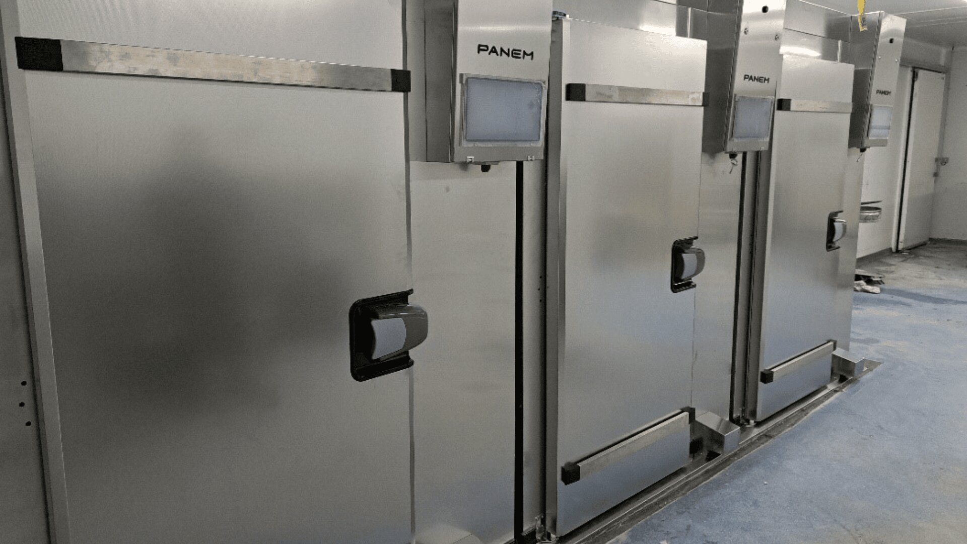 Three large stainless steel industrial machines with the brand name PANEM and digital screens are lined up against a wall in a clean, blue-floored room.