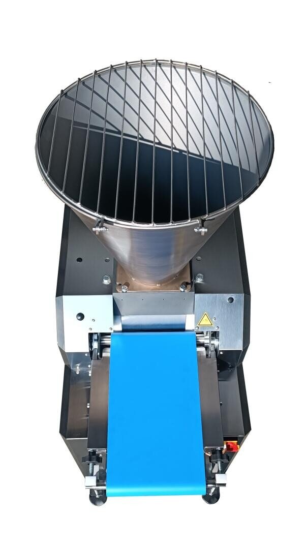 Industrial food processing machine with a large cylindrical hopper, metal grate on top, and a blue conveyor belt extending from the front, set against a white background.