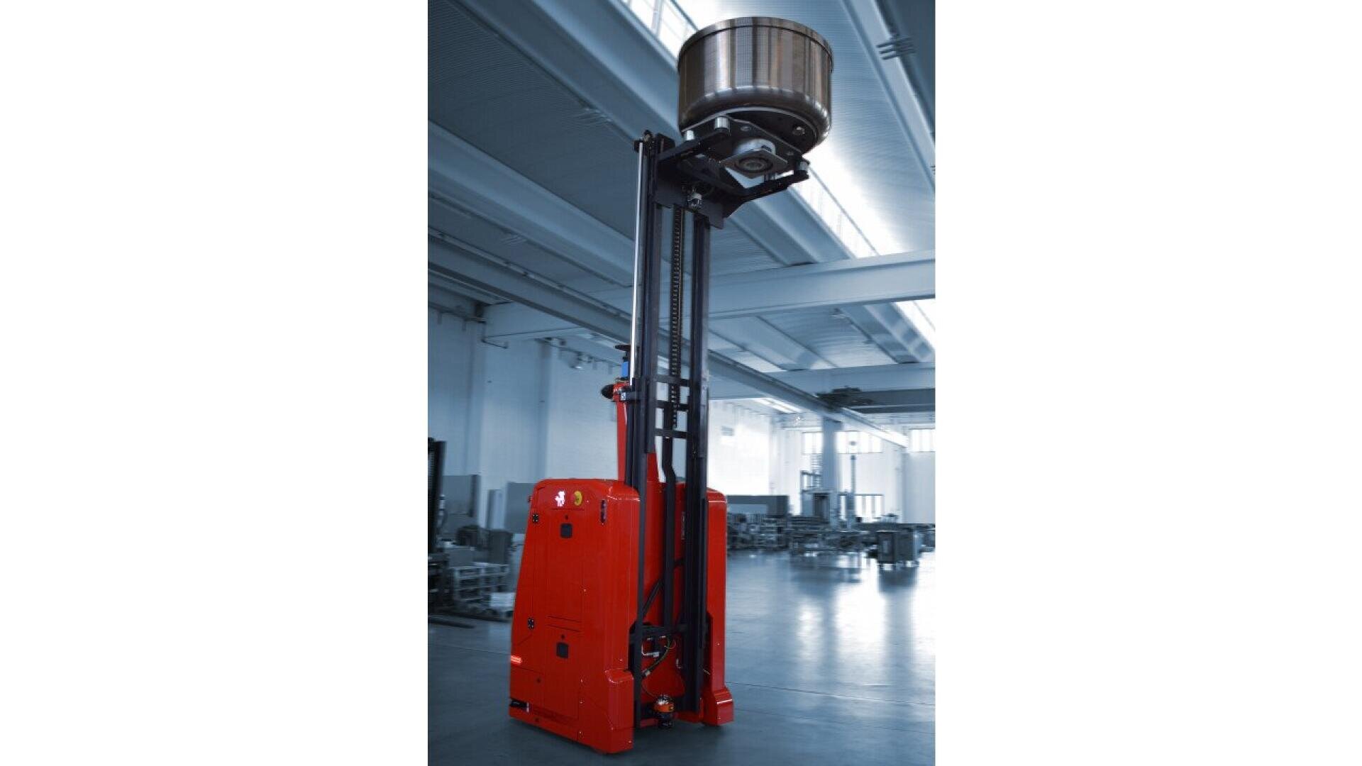 Ein roter automatischer Gabelstapler hebt ein großes Metallfass an seinem ausgefahrenen Mast hoch in ein geräumiges, industrielles Lager mit hohen Decken und heller Beleuchtung.