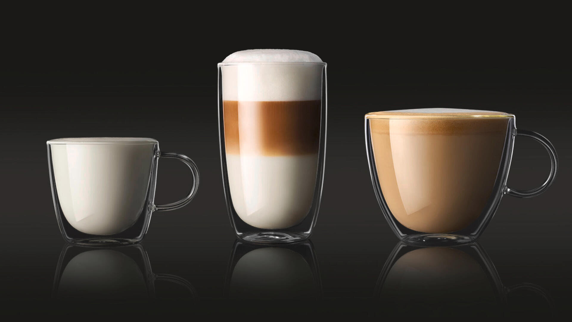 Drei klare Glastassen mit verschiedenen Kaffeegetränken stehen nebeneinander: eine kleine Tasse Milch, ein großer geschichteter Latte mit Schaum und eine mittelgroße Tasse hellbraunen Kaffees, alle auf schwarzem Hintergrund.