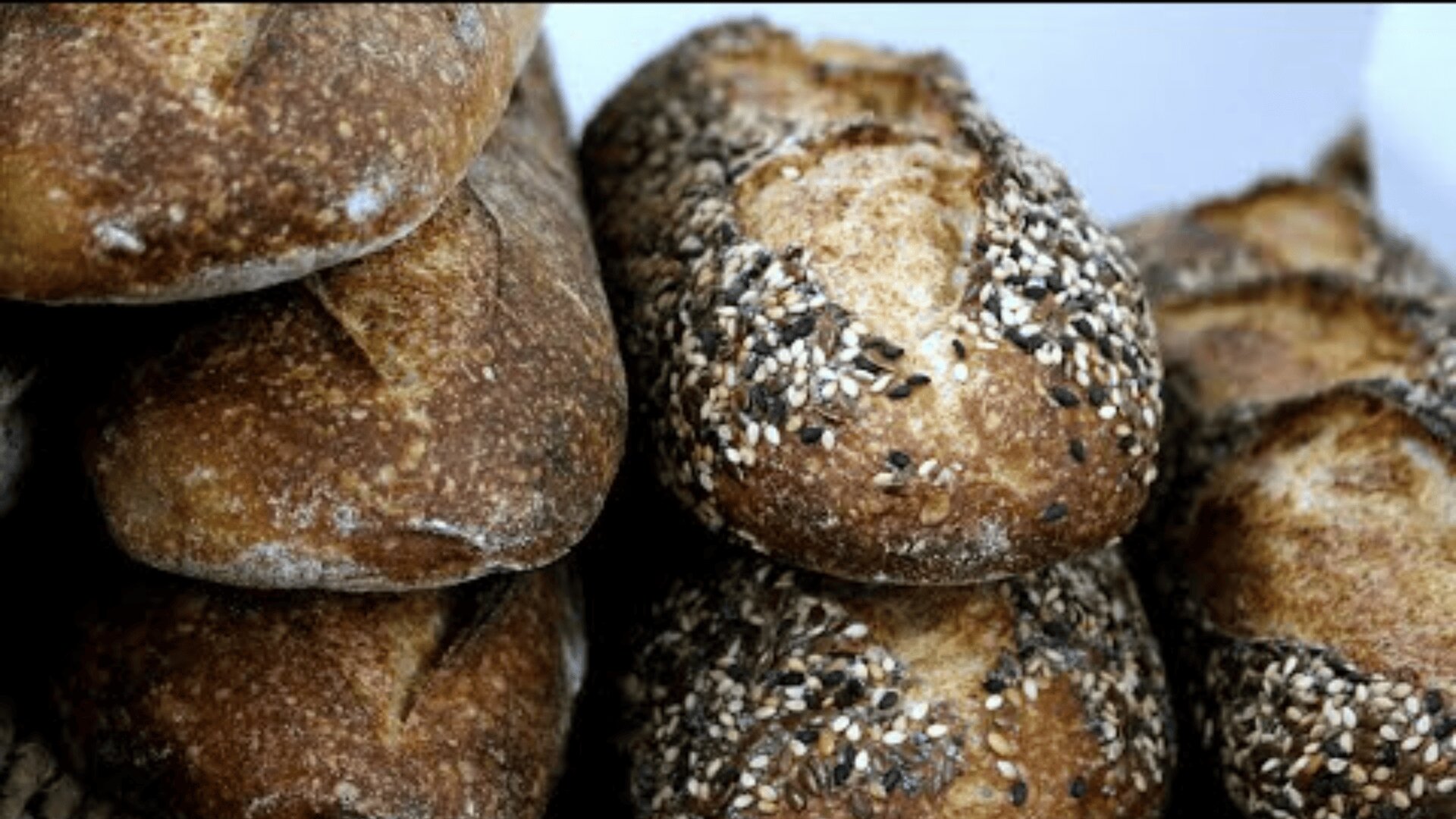 Rustikale Brotlaibe, die übereinander gestapelt sind, teilweise mit verschiedenen Körnern bestückt, haben eine knusprige, goldbraune Oberfläche.