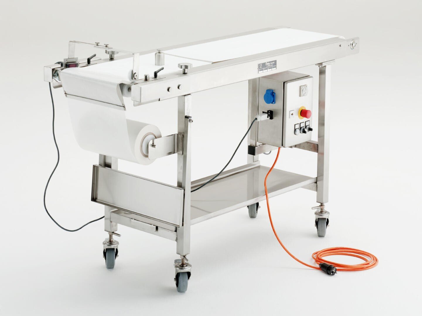 Eine Förderbandmaschine aus rostfreiem Stahl mit einem Bedienfeld, Rädern, einer weißen Materialrolle und einem orangefarbenen Stromkabel vor einem schlichten weißen Hintergrund.