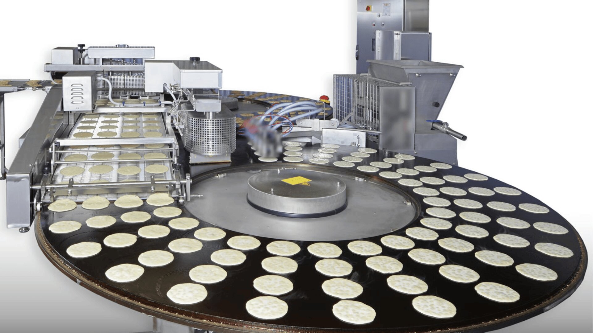 Eine große Industriemaschine verarbeitet und ordnet Reihen von runden, flachen Teiglingen auf einem Fördersystem in einer Lebensmittelproduktionsanlage an.