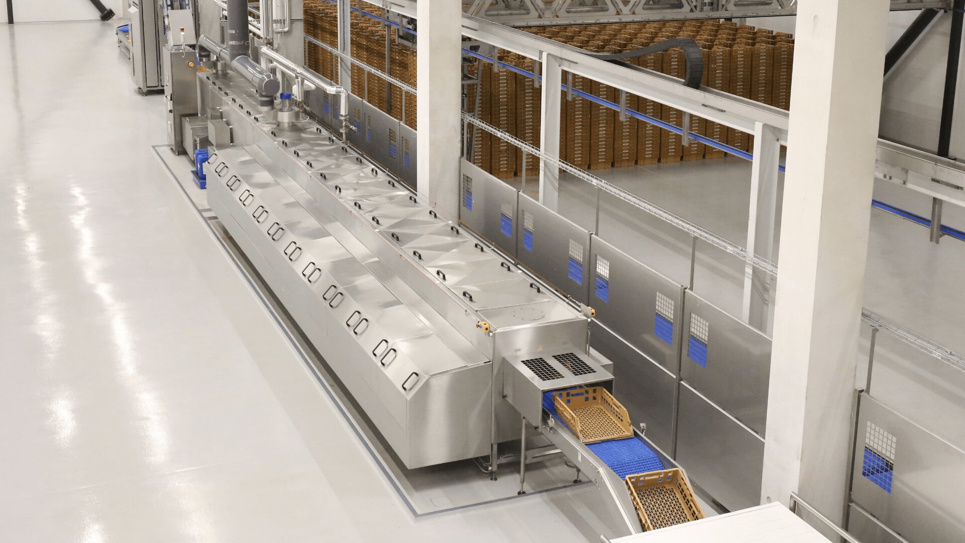 Eine moderne industrielle Lebensmittelverarbeitungsanlage mit Geräten aus Edelstahl und Förderbändern, die Schalen transportieren. Im Hintergrund stapeln sich Weidenkörbe auf einem sauberen, reflektierenden weißen Boden.