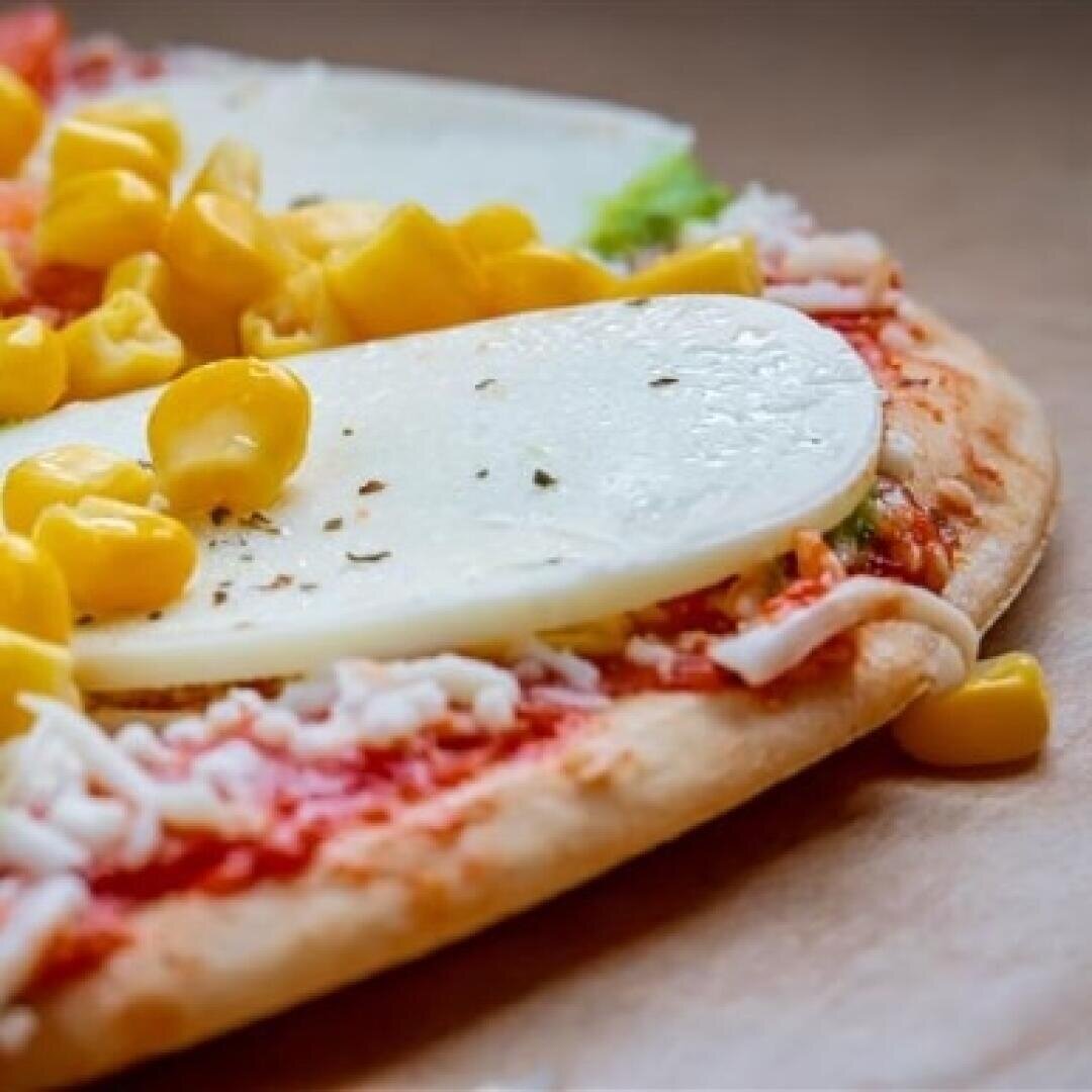 A close-up of a pizza topped with tomato sauce, shredded cheese, slices of mozzarella, and yellow corn kernels, resting on a brown surface.