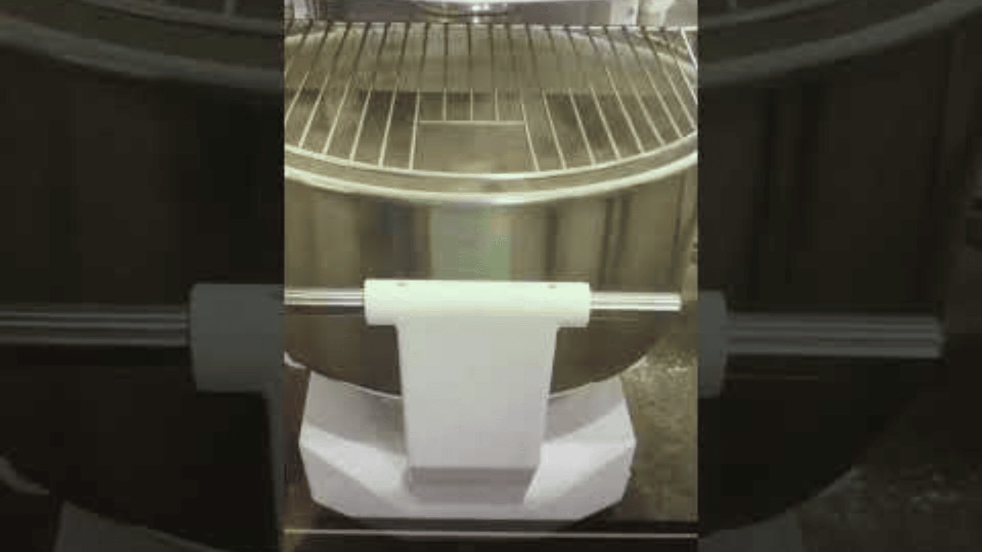 A close-up view of a commercial stand mixer with a large metal bowl and a protective wire guard on top, mounted on a white base.