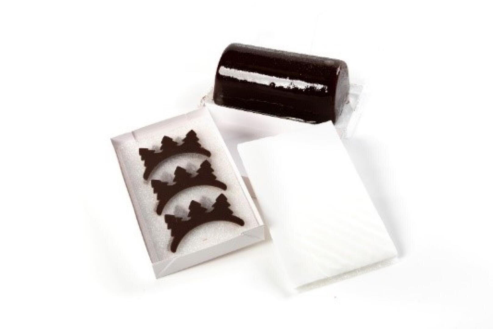 A glossy, dark chocolate cylinder is shown next to a white tray holding three chocolate crescent shapes and a white rectangular piece of paper.