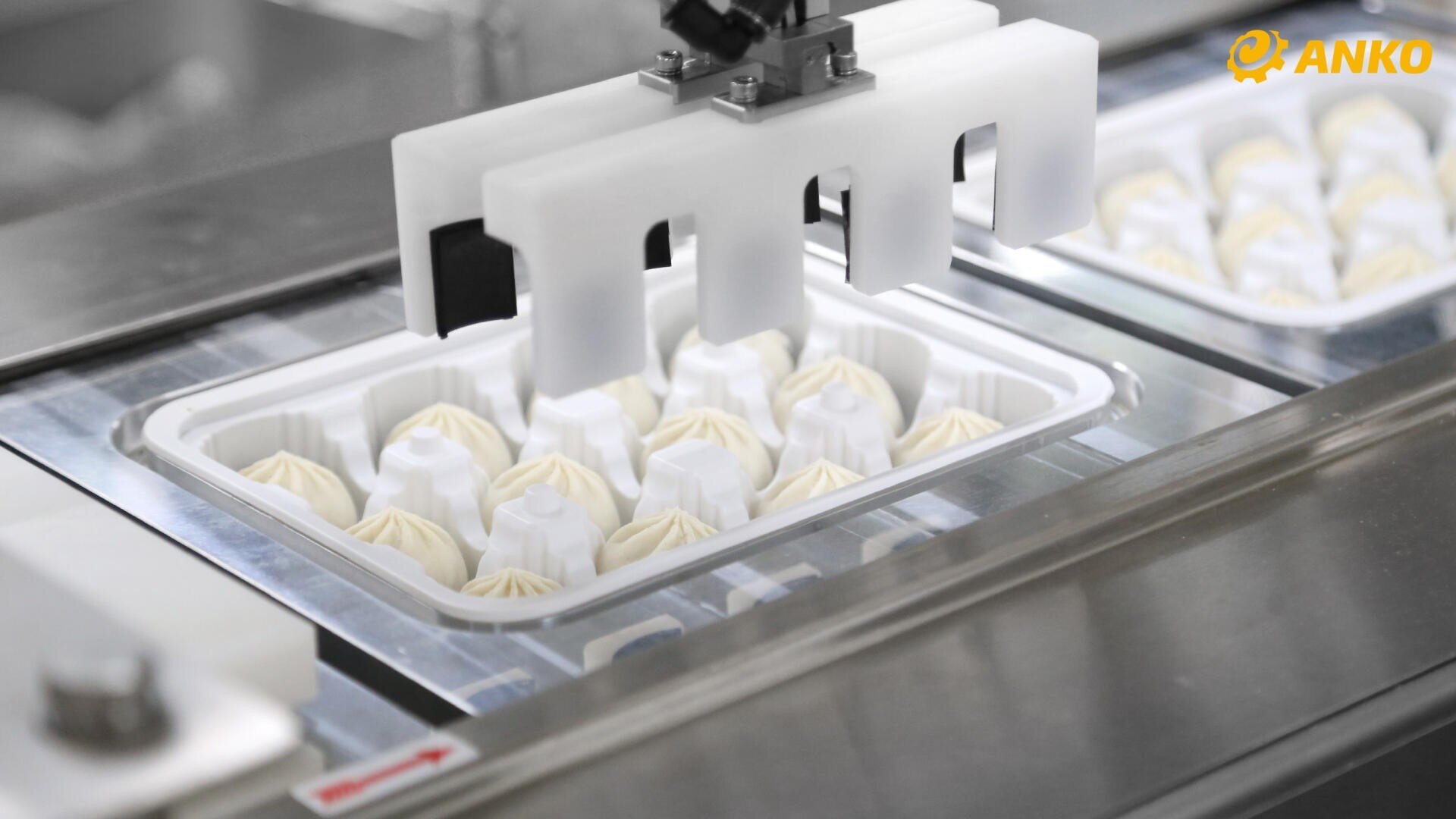 Close-up of a food production machine placing neatly arranged dumplings in a plastic tray. The ANKO logo can be seen in the top right-hand corner.