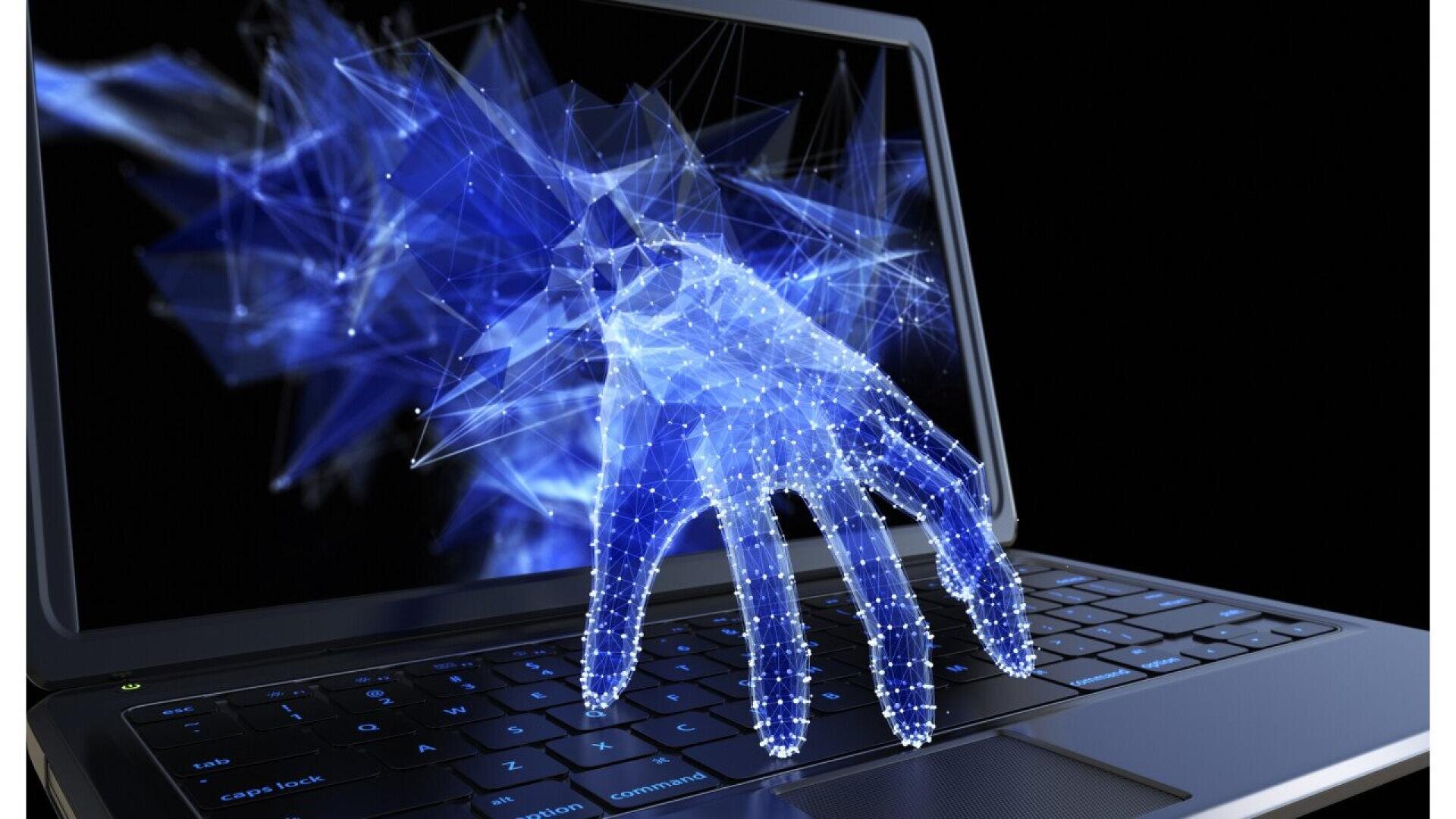 A digital, glowing blue hand made of points and lines reaches out from a laptop screen, symbolizing cybercrime or hacking. The scene is set against a dark background.
