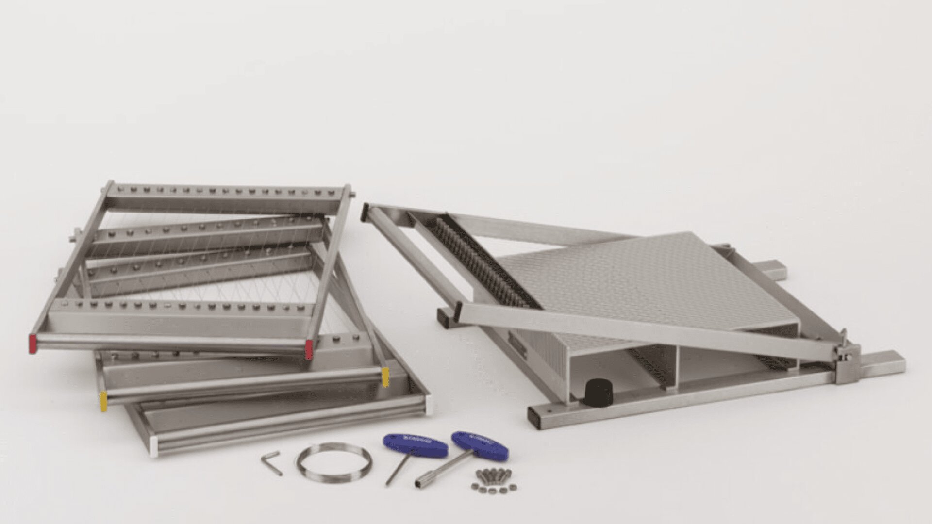 Disassembled metal platform lift with separate frame parts, screws, washers, two blue-handled screwdrivers, and a silver band, all arranged on a white surface.