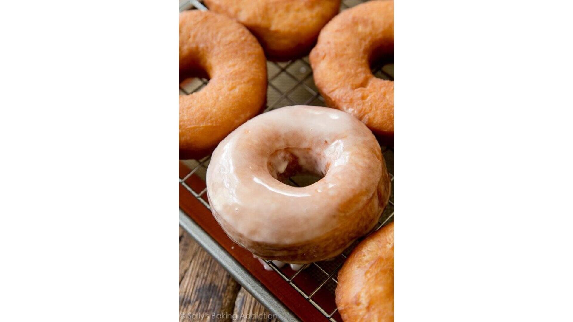 Eine Nahaufnahme von mehreren Donuts auf einem Kühlregal, wobei ein Donut in der Mitte mit glänzender Glasur überzogen ist, während die anderen glatt sind.