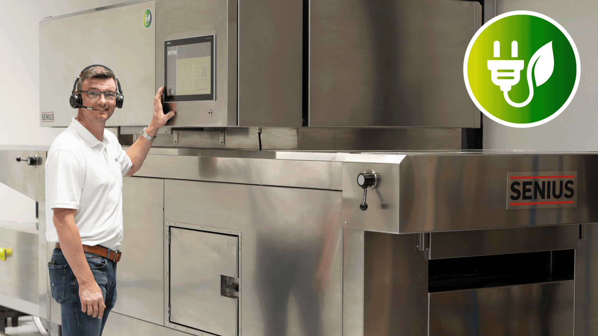 Ein Mann, der ein Headset und ein weißes Hemd trägt, bedient einen Touchscreen an einer großen Maschine aus Edelstahl mit der Aufschrift SENIUS. In der oberen rechten Ecke erscheint ein umweltfreundliches Stecker- und Blattsymbol.