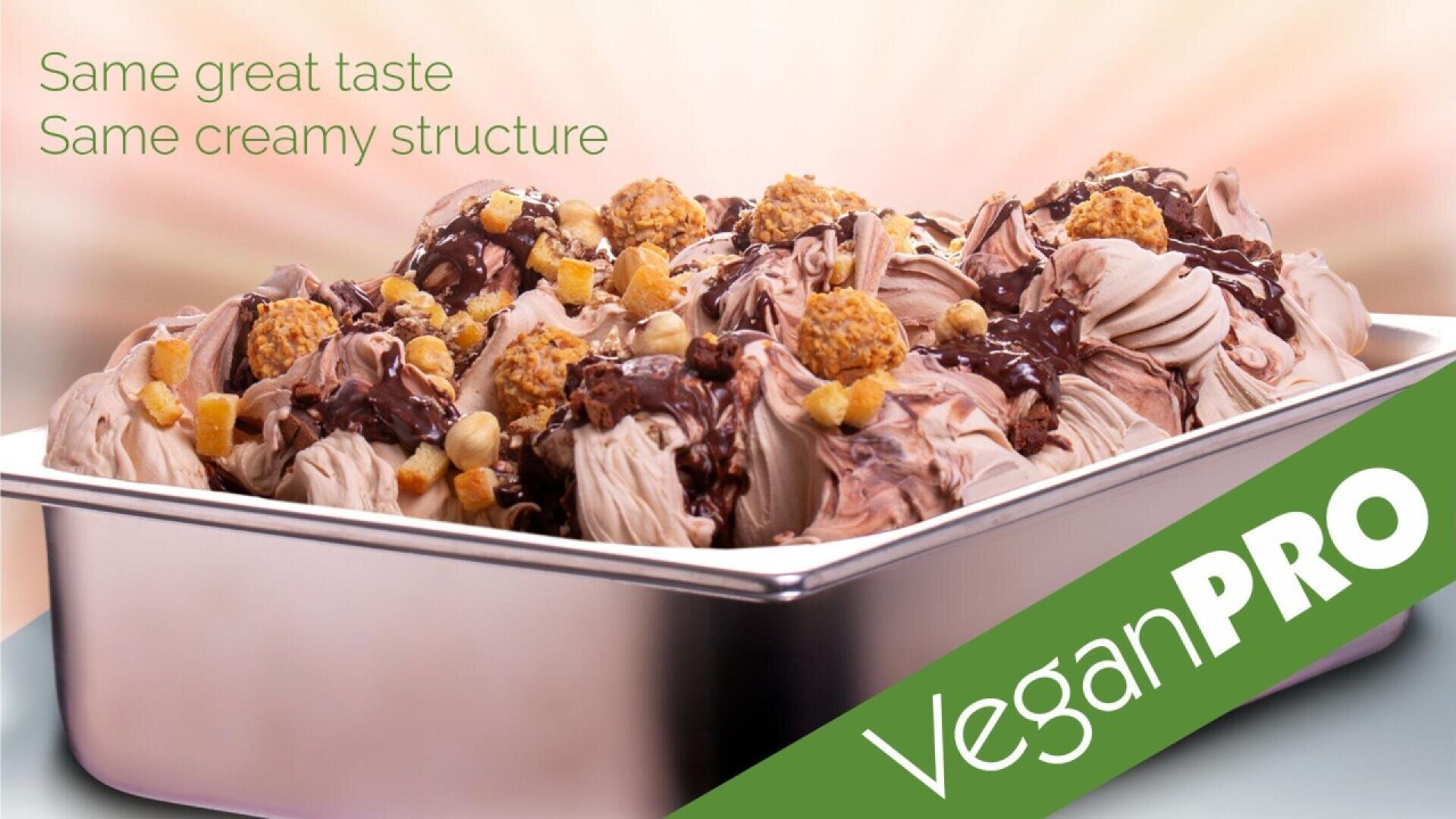 Eine Schale mit cremigem veganem Schokoladeneis, garniert mit Schokoladensauce, Nüssen und Keksstückchen. Grüner Text: „Gleicher toller Geschmack, gleiche cremige Konsistenz.“ Auf einem grünen Banner steht „Vegan PRO“.