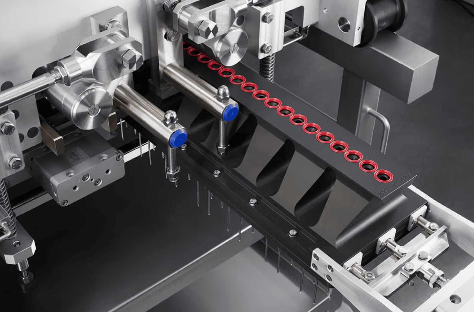 Nahaufnahme einer automatisierten pharmazeutischen Maschine, die mehrere kleine Fläschchen mit Flüssigkeit füllt. Die Fläschchen sind in einer schwarzen Schale ausgerichtet, und Metallteile mit Schläuchen und Düsen sind sichtbar.