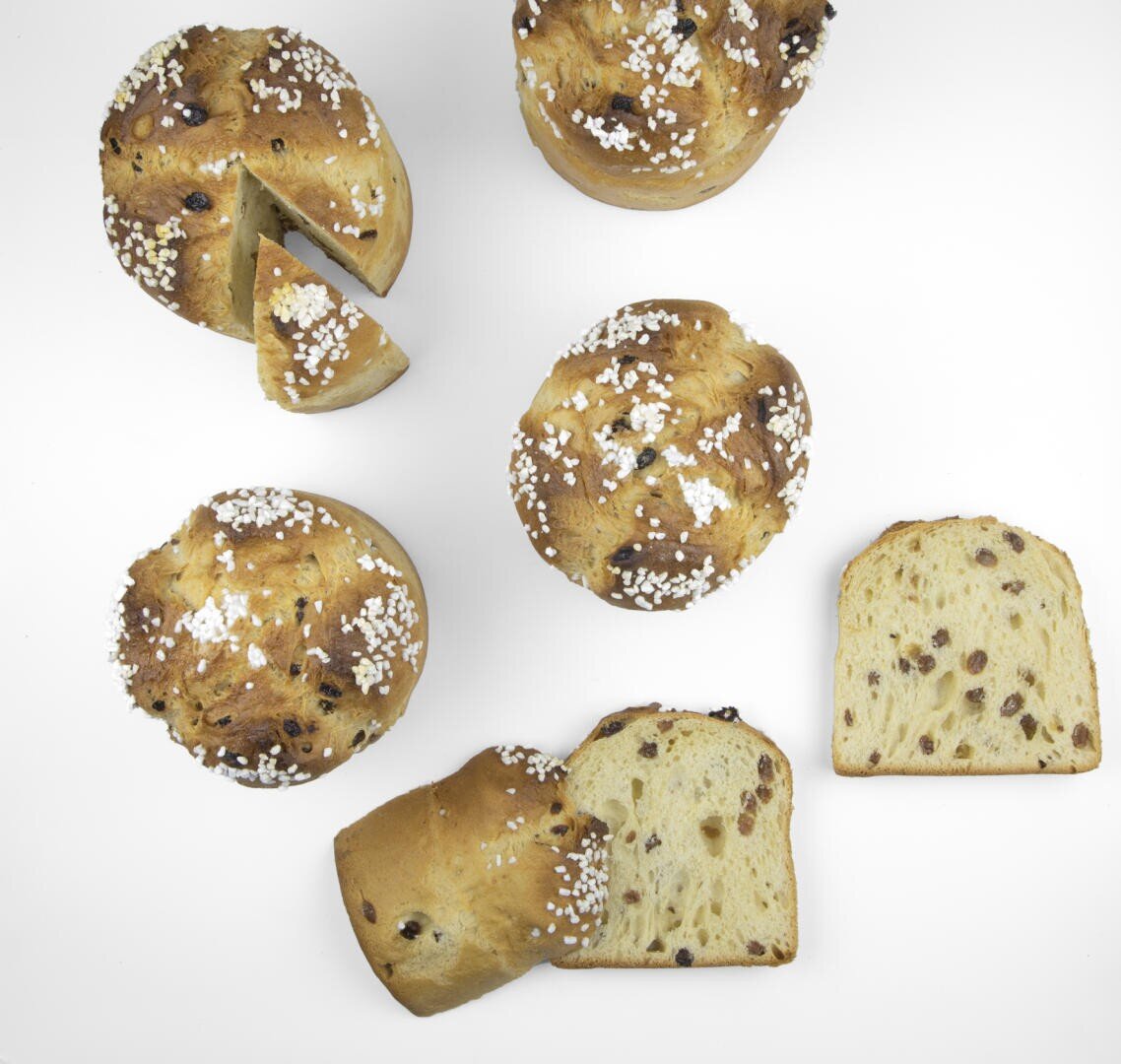 Draufsicht auf mehrere runde Brote mit weißen Zuckerkristallen auf der Oberseite, einige ganz und einige in Scheiben geschnitten, mit ein paar einzelnen Scheiben in der Nähe auf einem weißen Hintergrund.