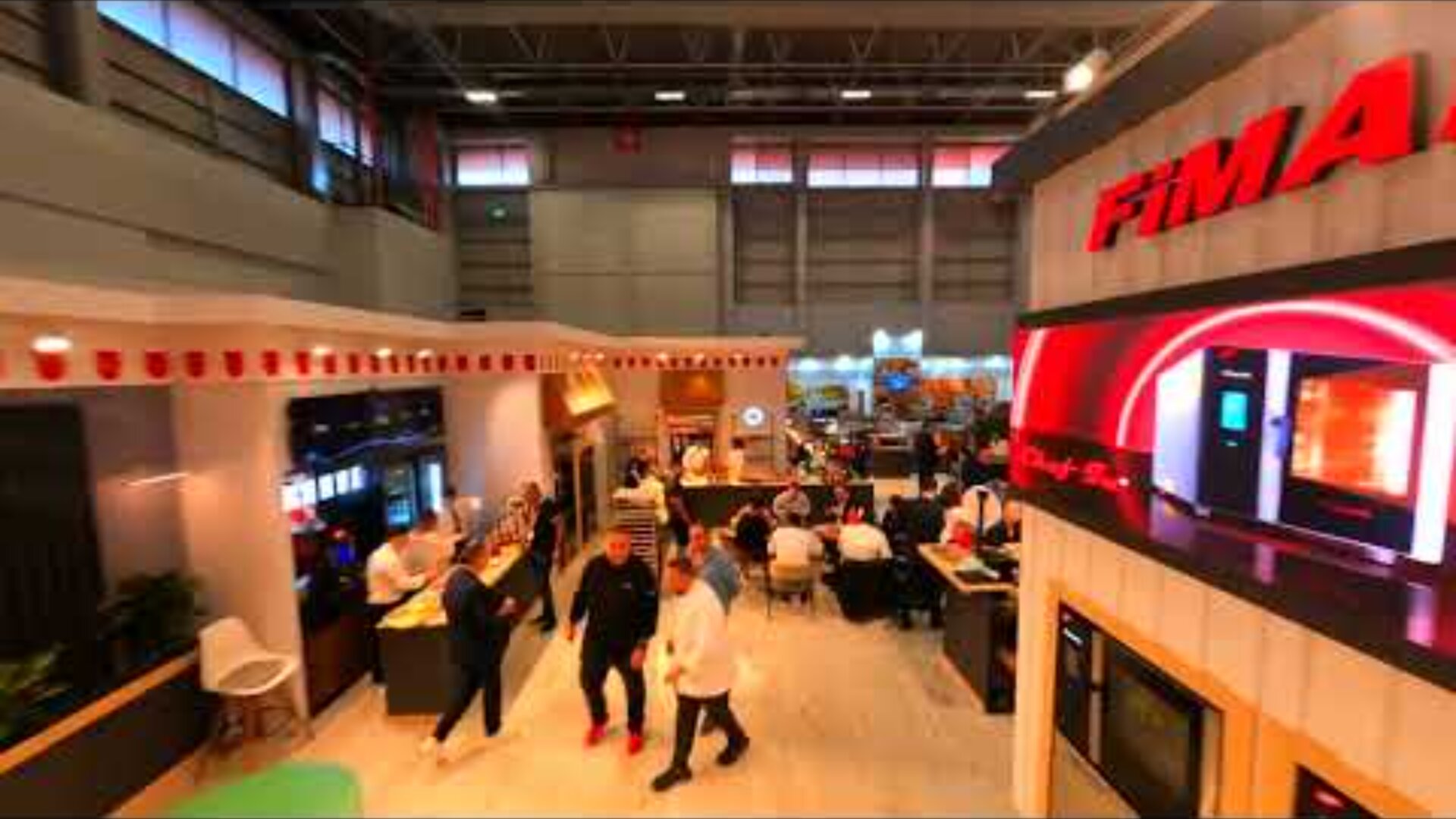 A busy trade show or exhibition hall with people walking and sitting at tables, various booths, digital displays, and a large FIMAR sign on the right. Bright lighting and modern decor are visible throughout the space.