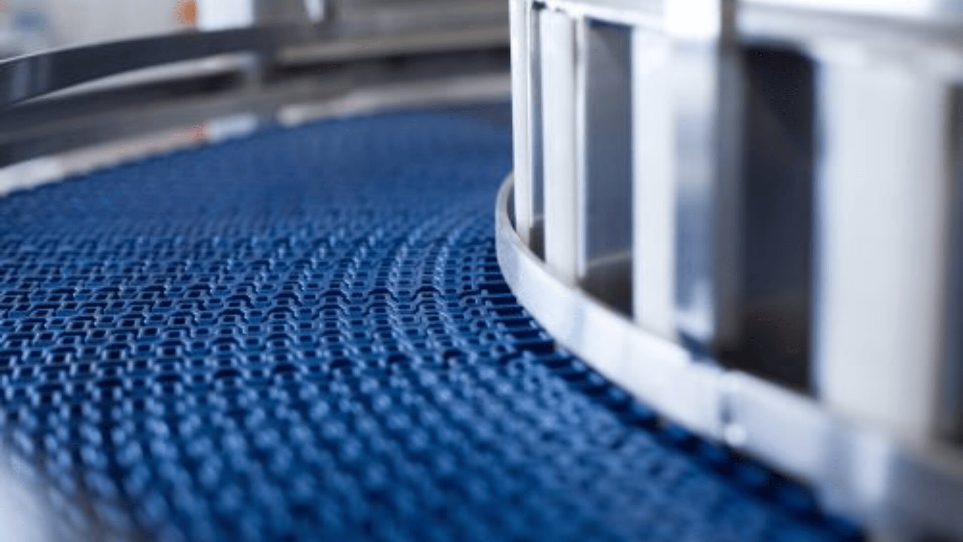 A close-up view of a blue conveyor belt with a textured surface, curving around a metal frame in an industrial setting.