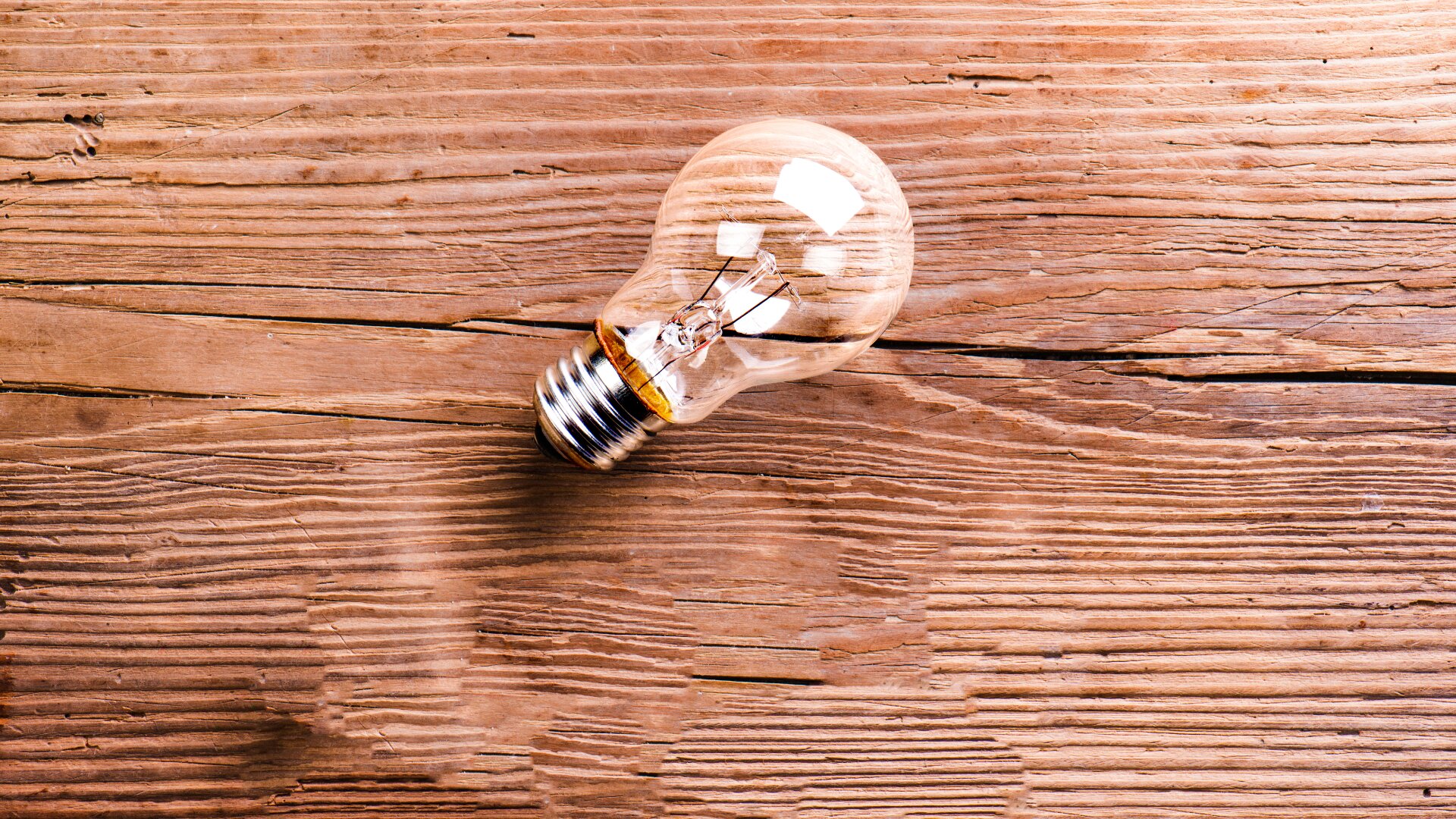 Eine klare Glühbirne liegt auf der Seite auf einer strukturierten Holzoberfläche mit sichtbarer Maserung und Linien.