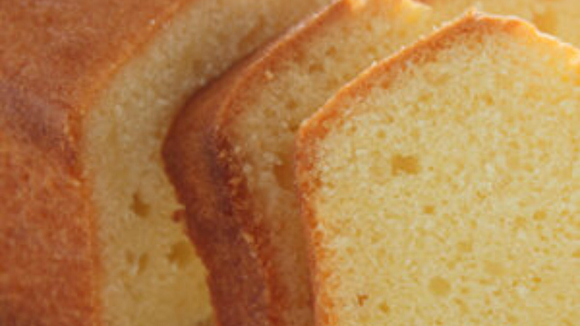 Nahaufnahme mehrerer Scheiben goldbraunen, saftigen Pfundkuchens mit weicher, krümeliger Textur und leicht gebräunten Rändern.