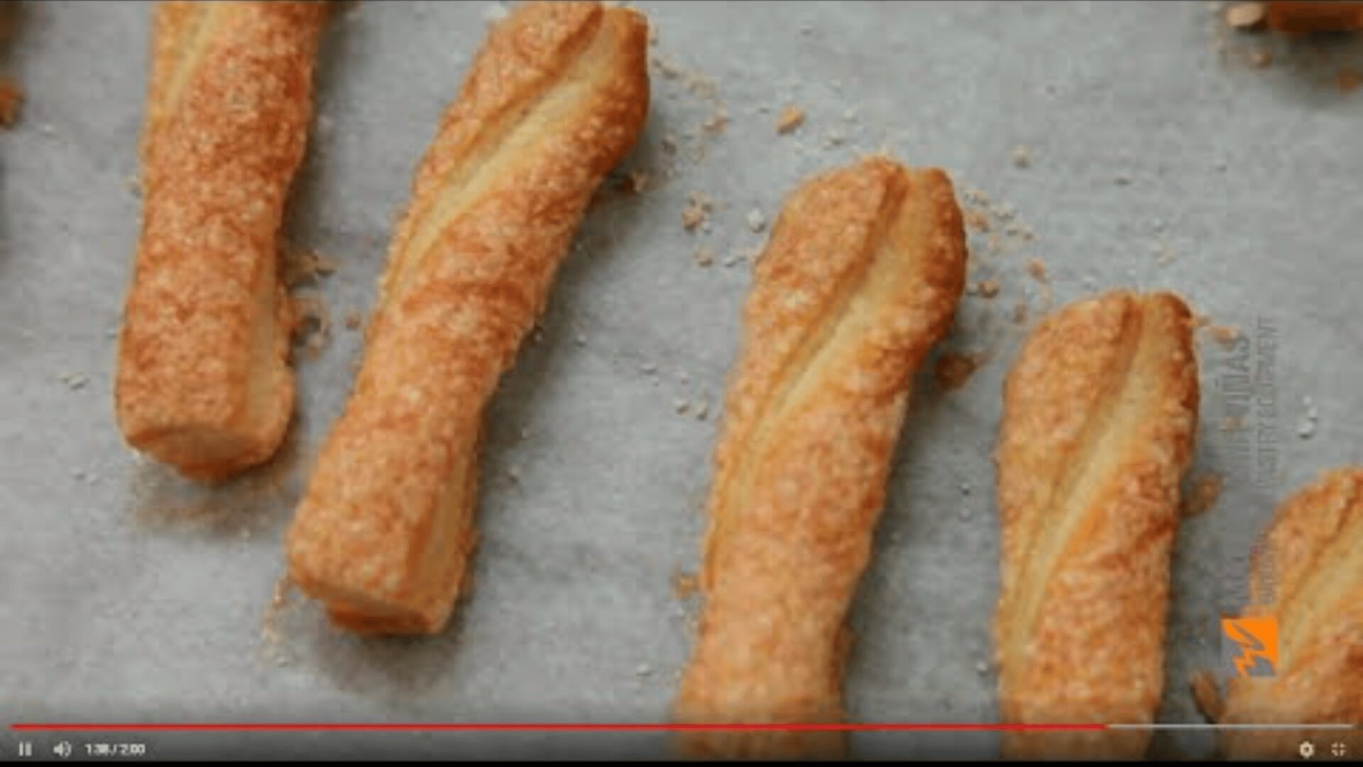 Place golden-brown, twisted pastry sticks sprinkled with sugar on a baking tray lined with parchment paper. Sprinkle a few crumbs around the cookies.
