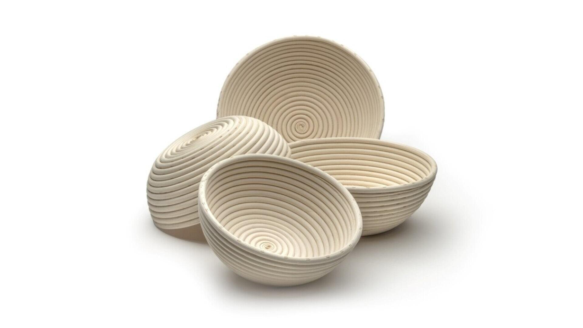 Four round, off-white, spiral-patterned proofing baskets are arranged together on a plain white background. Three baskets are nested or stacked, while one is positioned upright, showing the interior spiral design.