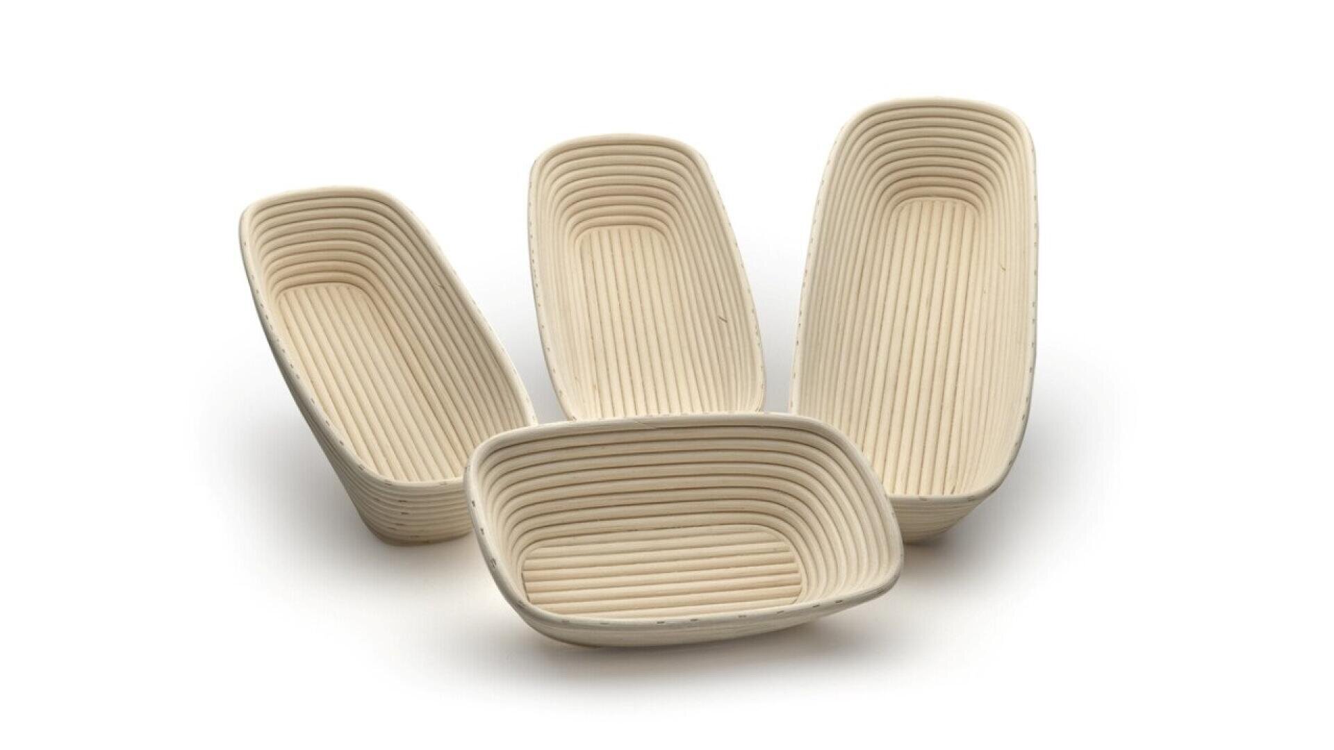 Four rectangular, ribbed proofing baskets made of light-colored wicker are arranged together on a white background, with three standing upright and one lying on its side in the front.