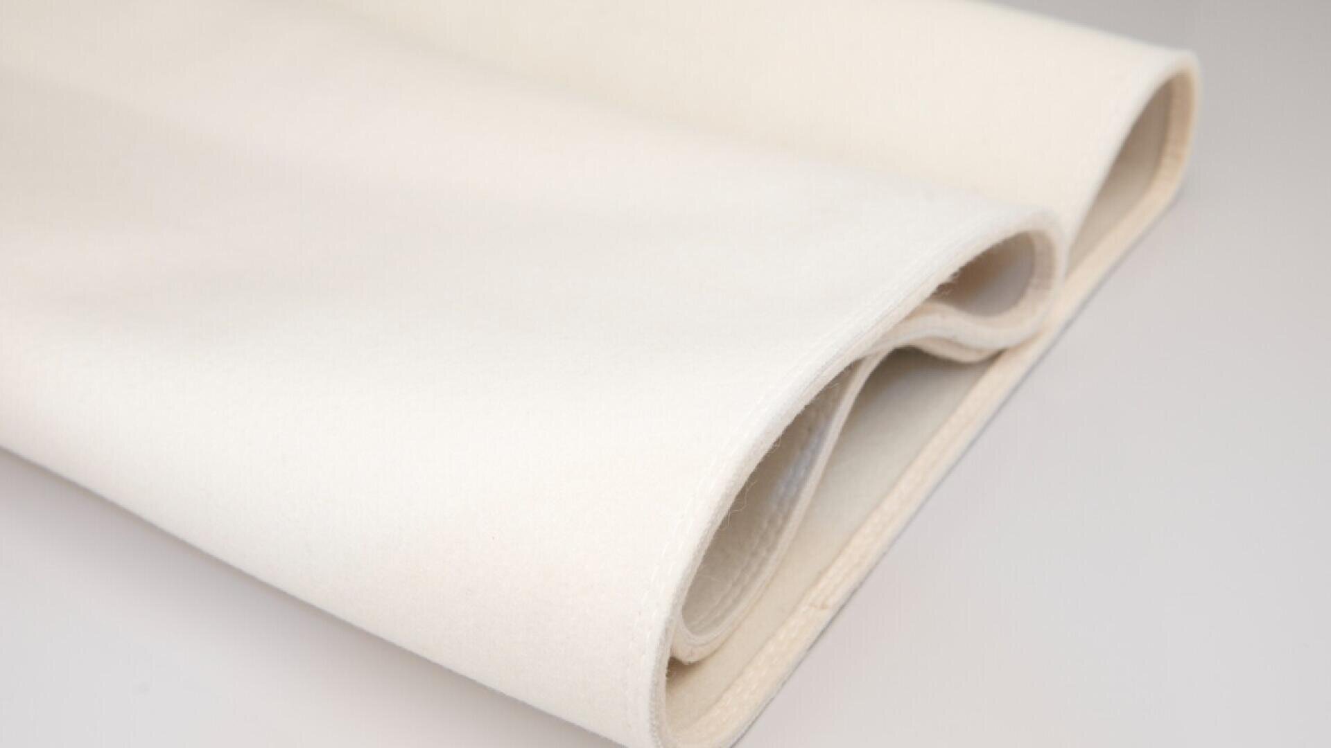 A close-up of two folded pieces of off-white felt fabric, placed on a smooth, light-colored surface.