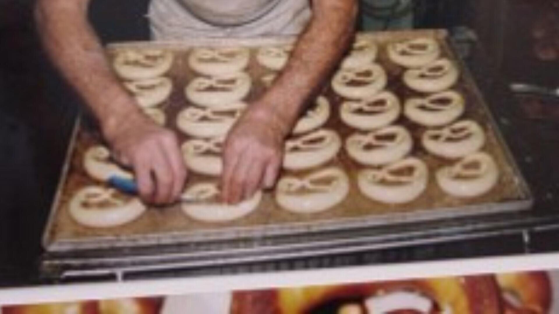 A person shapes pretzel dough on a baking tray, arranging the dough into the classic pretzel form before baking.