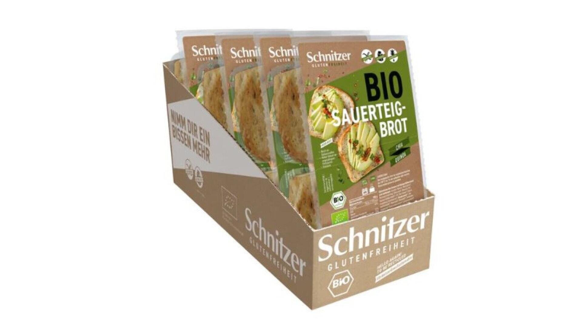 A cardboard display box holds several packages of Schnitzer Bio Sauerteig-Brot, a gluten-free organic sourdough bread, with green and brown packaging showing sliced bread and a bread plate.