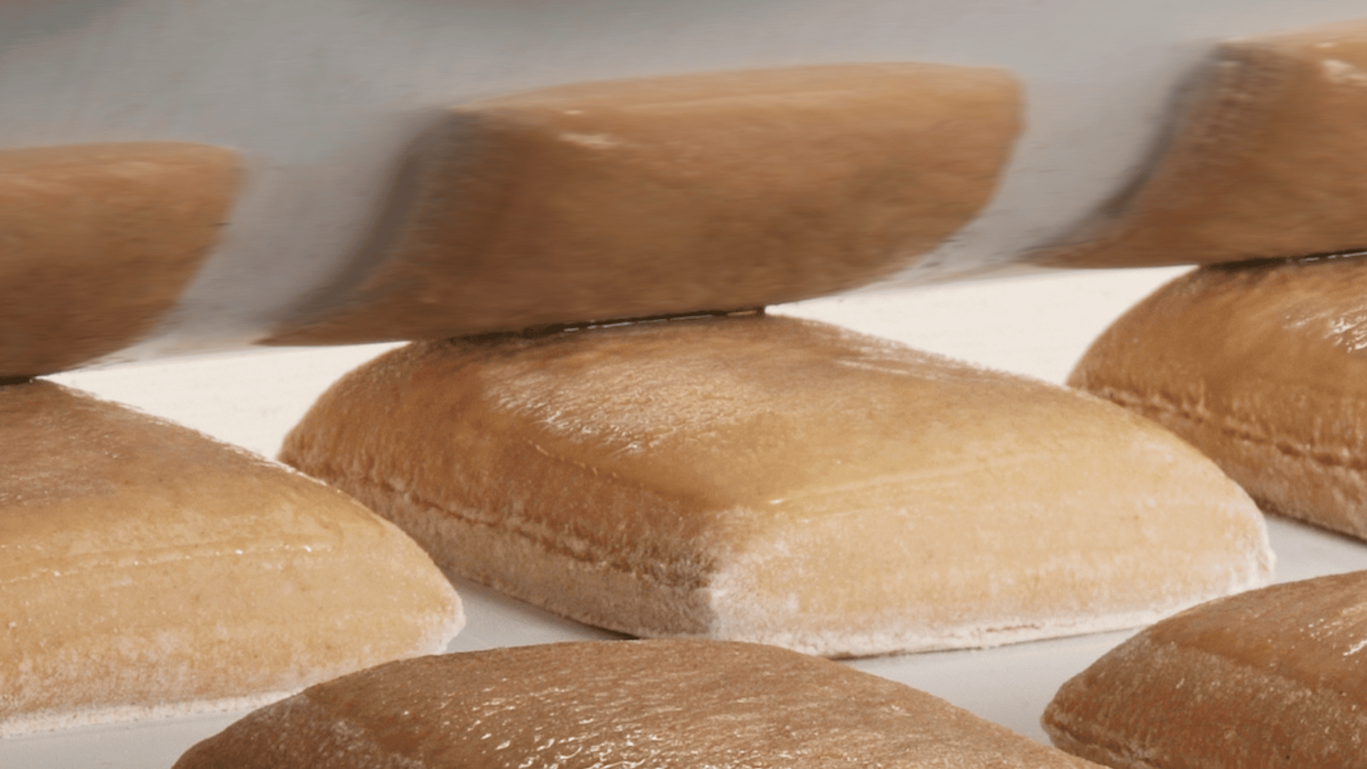 Close-up of a machine pressing down on rectangular pieces of dough on a white surface, preparing them for baking. The dough is lightly dusted with flour.