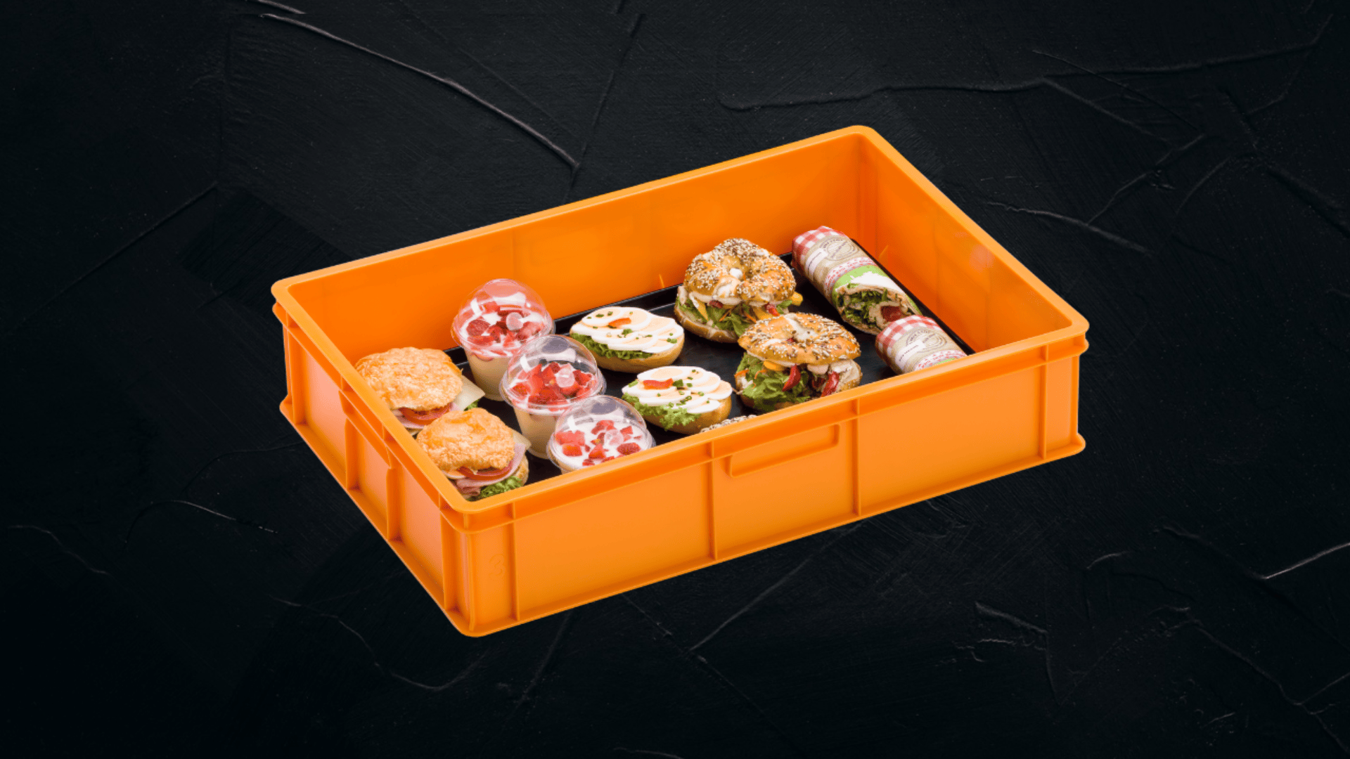Eine orangefarbene Plastikkiste enthält eine Auswahl an ordentlich angeordneten Sushi-Rollen und kleinen Sandwiches auf einer dunkel strukturierten Oberfläche.