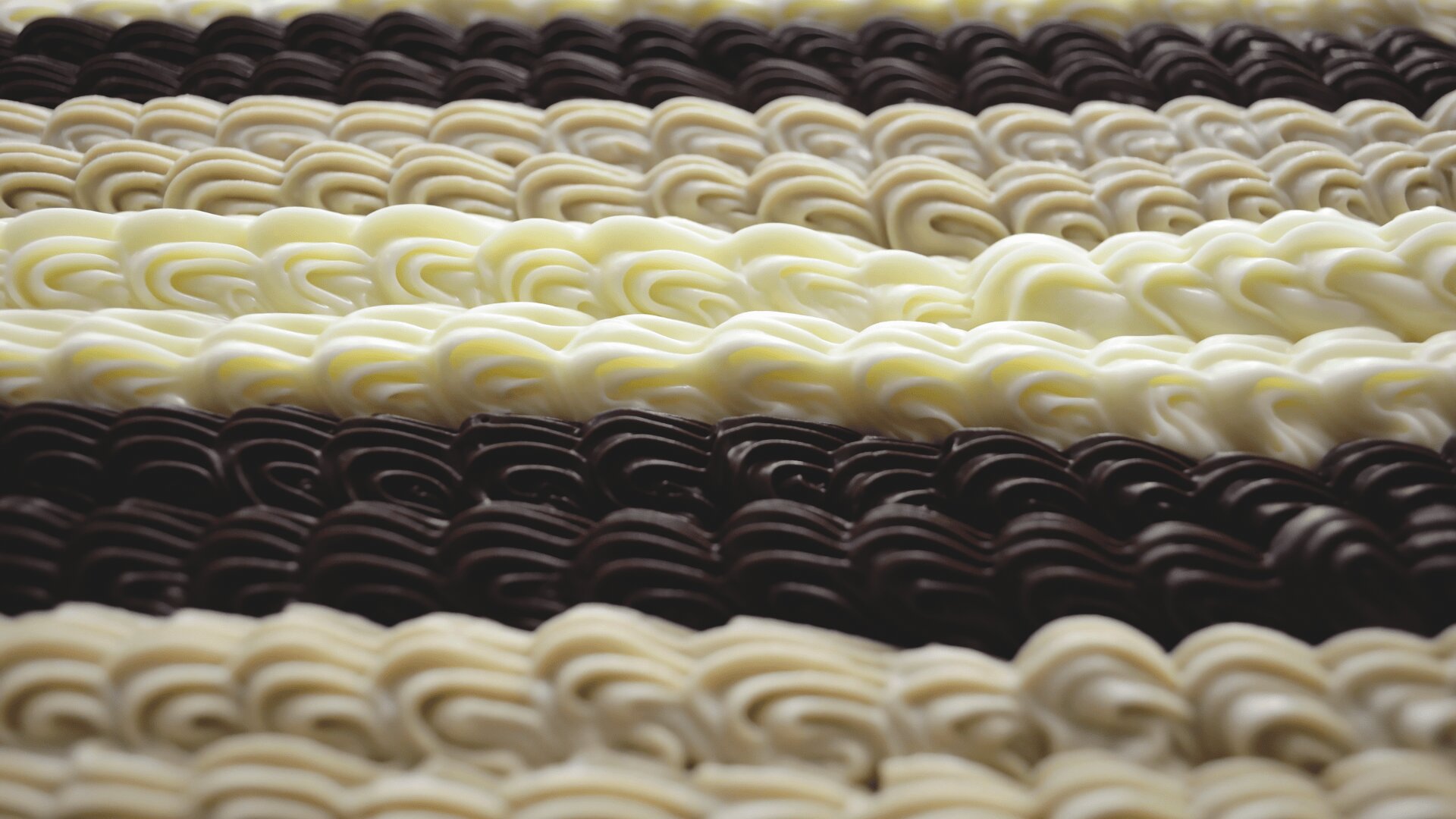 Close-up of alternating rows of white and dark chocolate piped in decorative, swirled patterns, creating a visually appealing, textured surface.