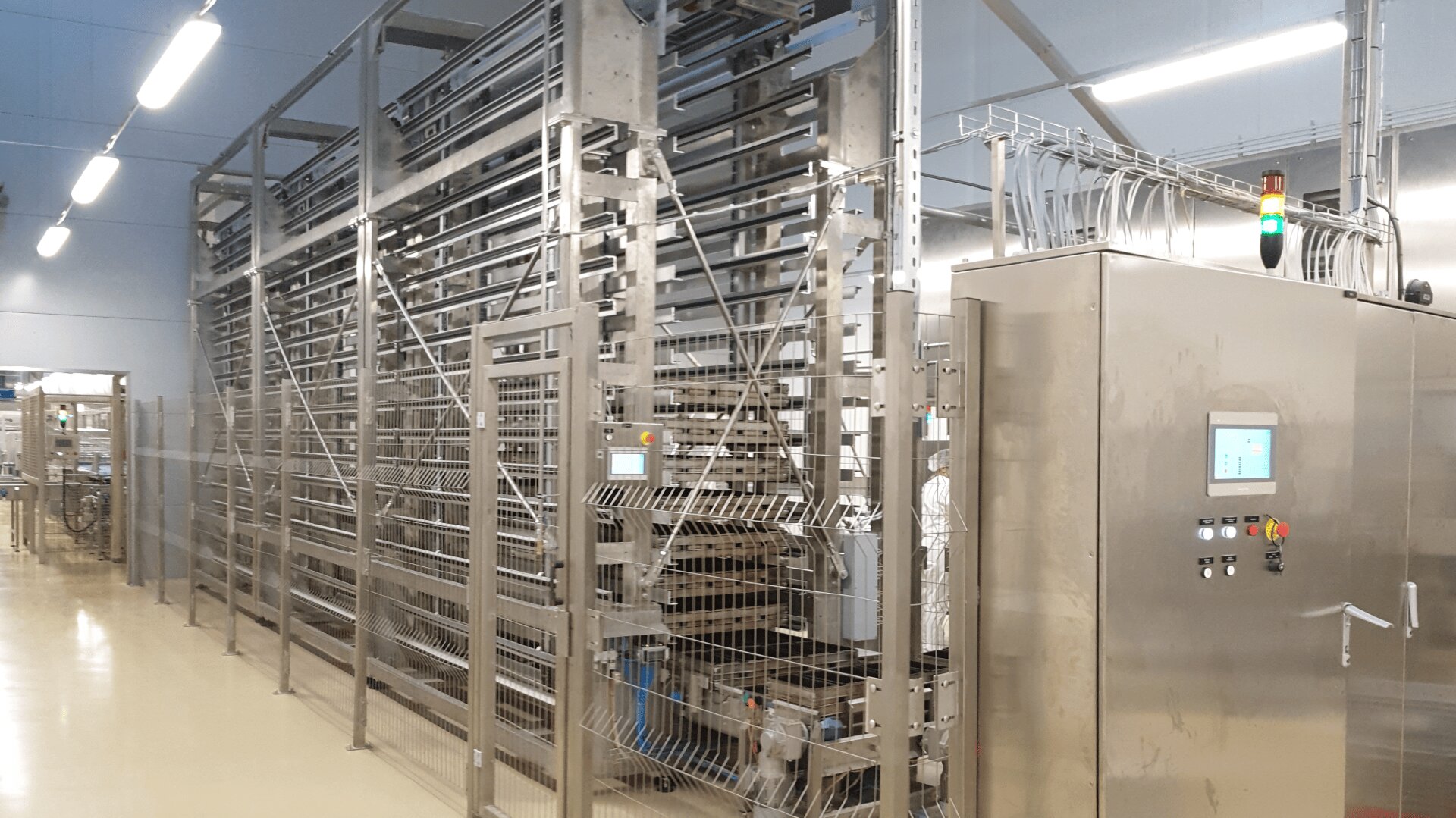 A modern industrial facility with stainless steel machinery, control panels, pipes, and cables. The area is brightly lit and clean, with a focus on automated processing equipment.