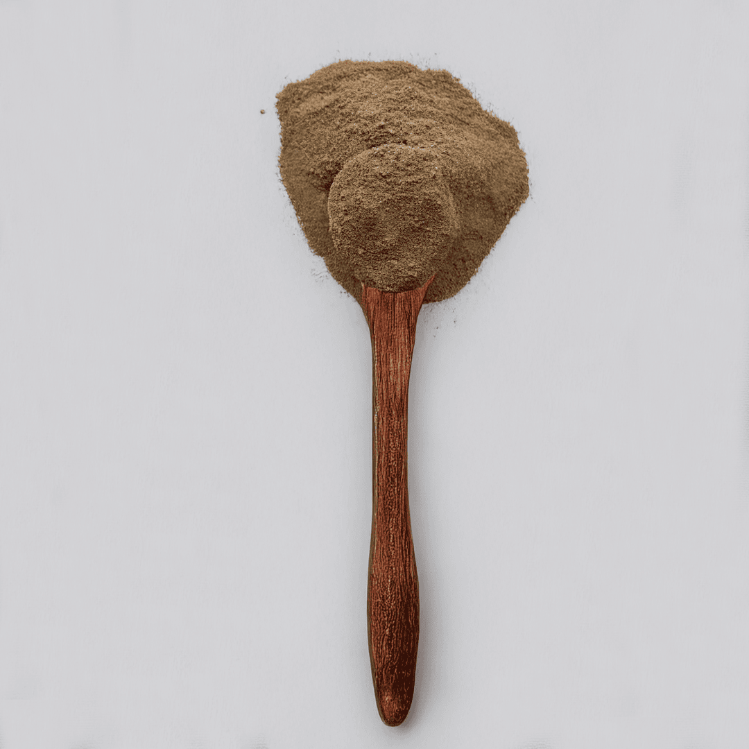 A wooden spoon filled with brown powder rests on a white surface, with extra powder scattered around the spoon.