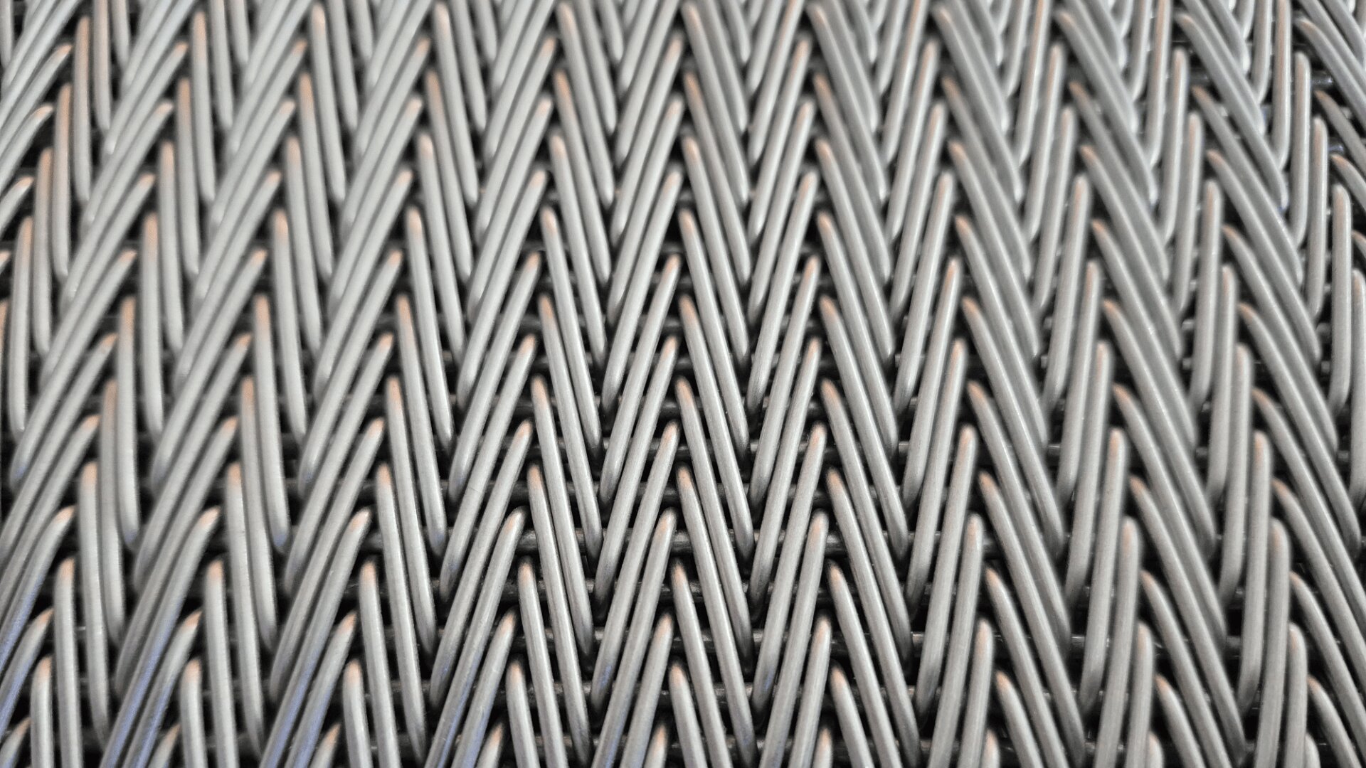 Nahaufnahme eines gewebten Musters aus verflochtenen grauen und braunen synthetischen Fasern, die in einem sich wiederholenden Chevron- oder Fischgrätenmuster angeordnet sind.