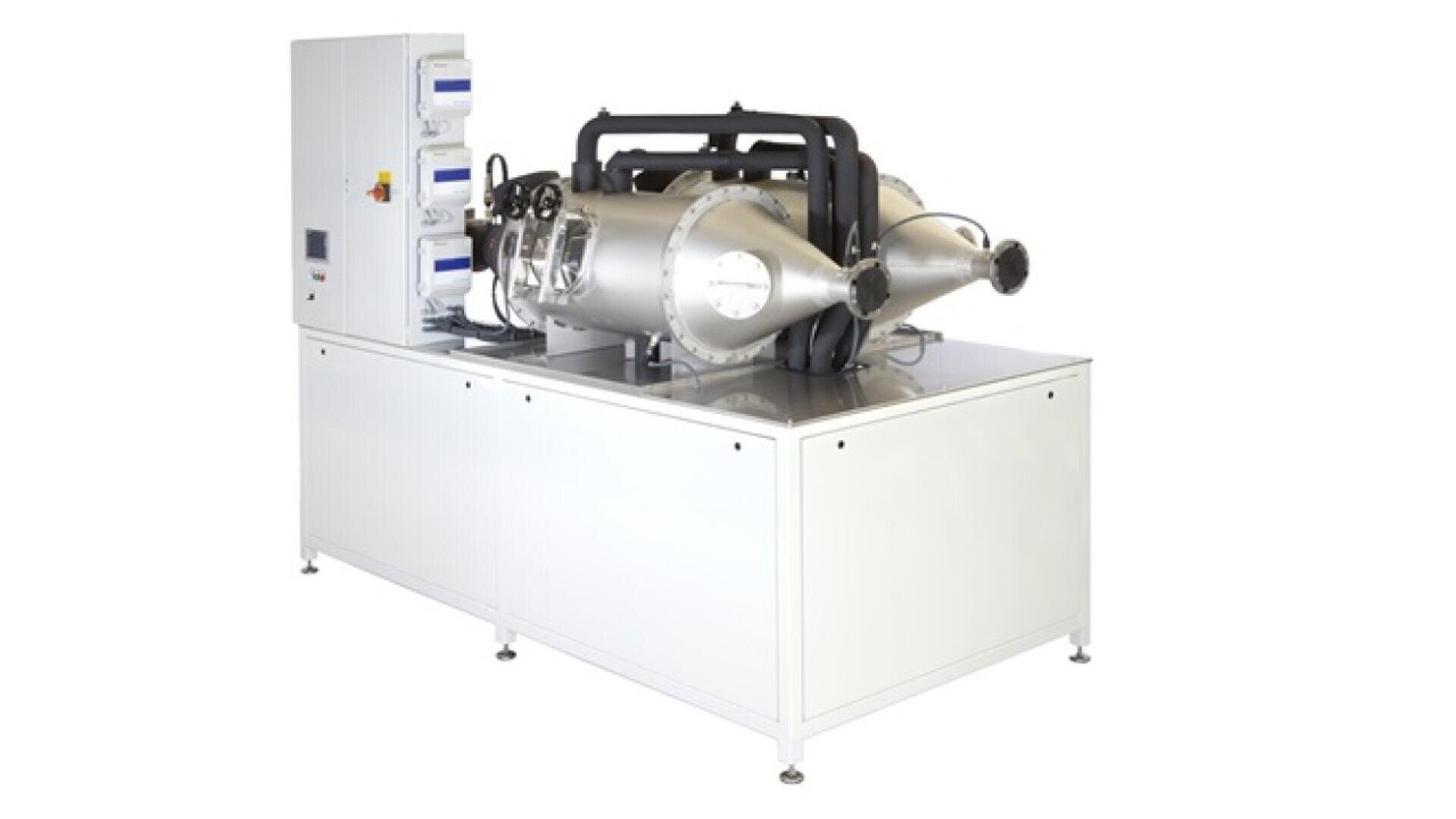 A large white laboratory machine with metal cylindrical chambers, control panels, and display screens, used for scientific or industrial processes, stands on a white base.