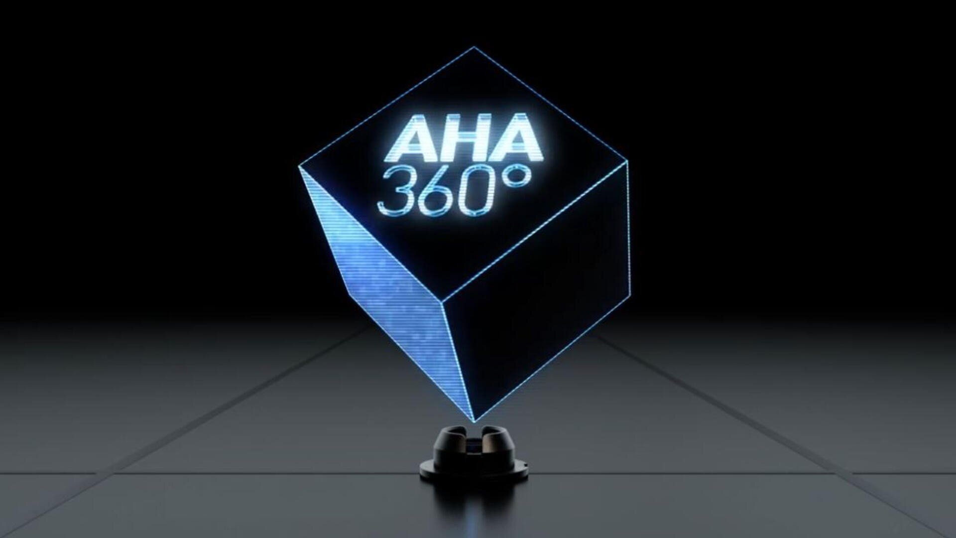 Ein leuchtender, durchscheinender, blauer 3D-Würfel mit dem Text „AHA 360°“ schwebt über einer dunklen, gittergemusterten Oberfläche, darunter projiziert ein kleines schwarzes Gerät das Hologramm.