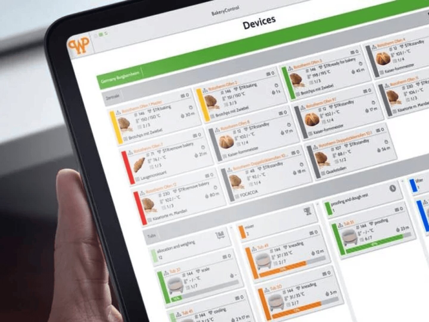 Eine Person hält ein Tablet in der Hand, auf dem ein Dashboard mit dem Titel "Geräte" zu sehen ist, das verschiedene Gerätestatuskarten in Reihen mit farbigen Balken, Symbolen und technischen Details auf dem Bildschirm anzeigt.
