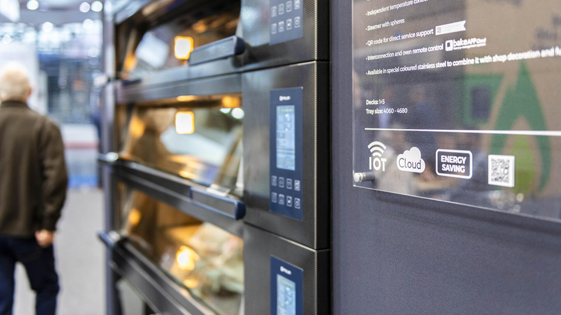 Close-up of a modern industrial furnace with digital controls and cloud connectivity icons in a commercial setting. A person can be seen walking away in the blurred background.