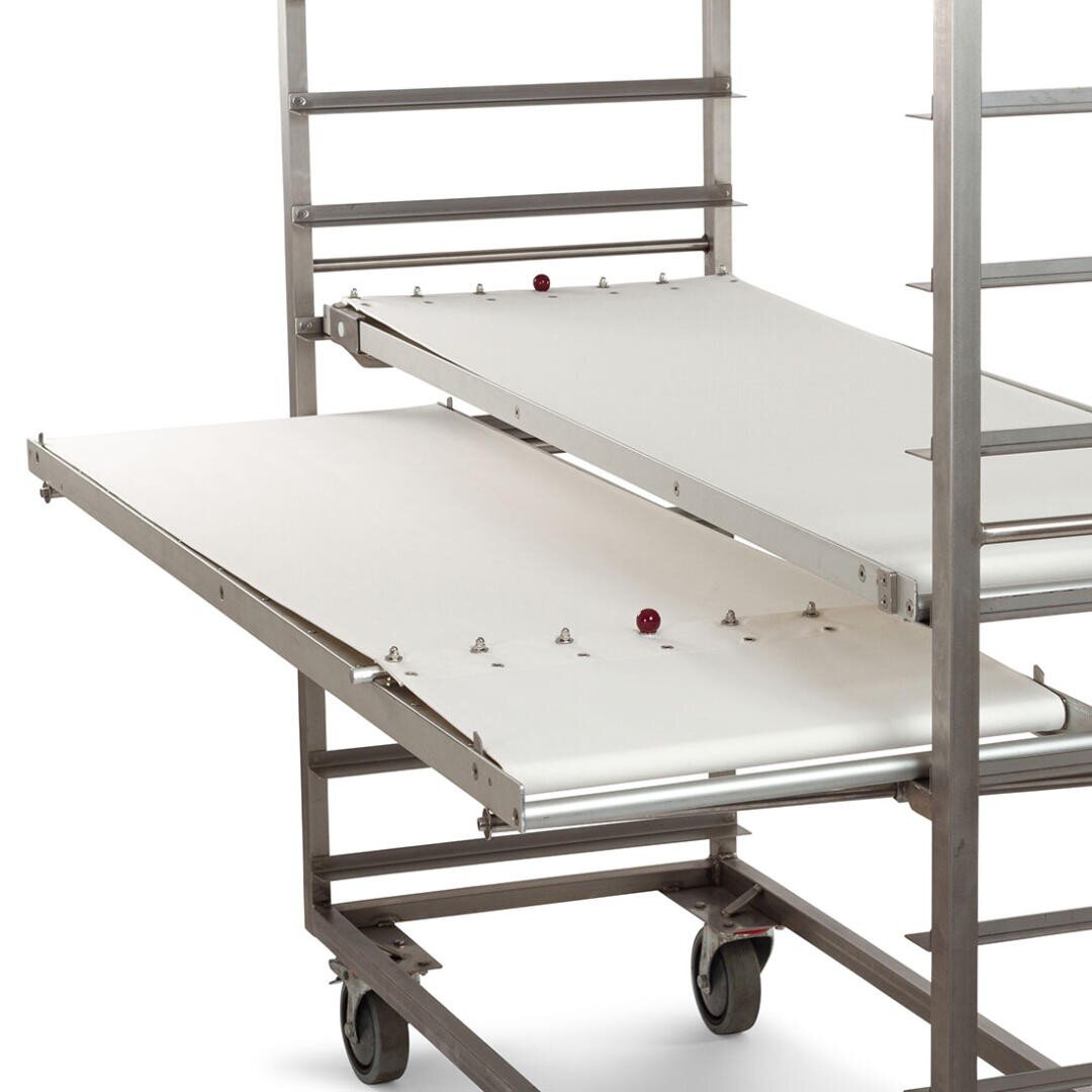 Ein Wagen aus rostfreiem Stahl mit mehreren Einlegeböden, von denen einer herausgezogen und mit einer weißen Oberfläche versehen ist. Der Wagen steht auf Rädern und hat kleine Metallstifte und rote Knöpfe, die auf den Regalböden sichtbar sind.