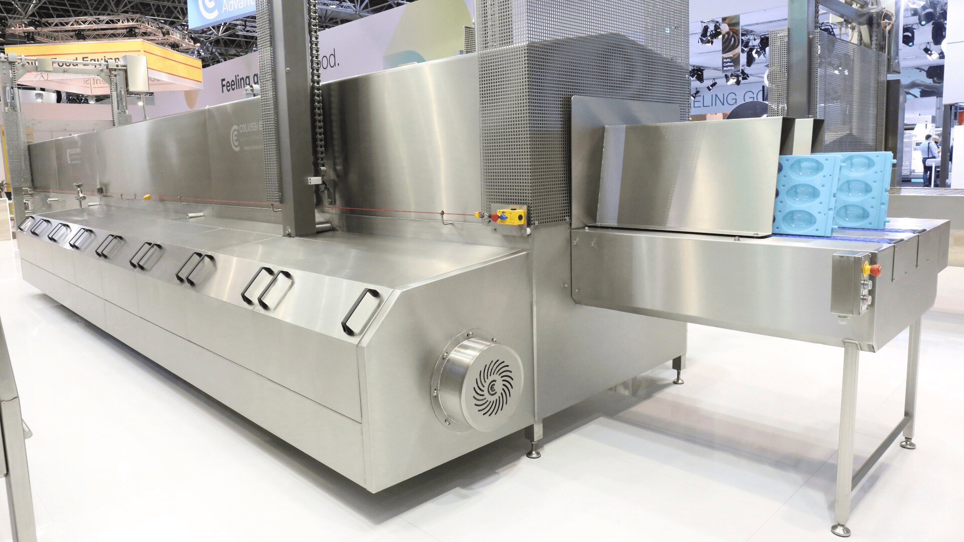 Große industrielle Lebensmittelverarbeitungsmaschine aus rostfreiem Stahl mit einem Förderband und blauen Silikonformen in einer sauberen, modernen Fabrikumgebung.